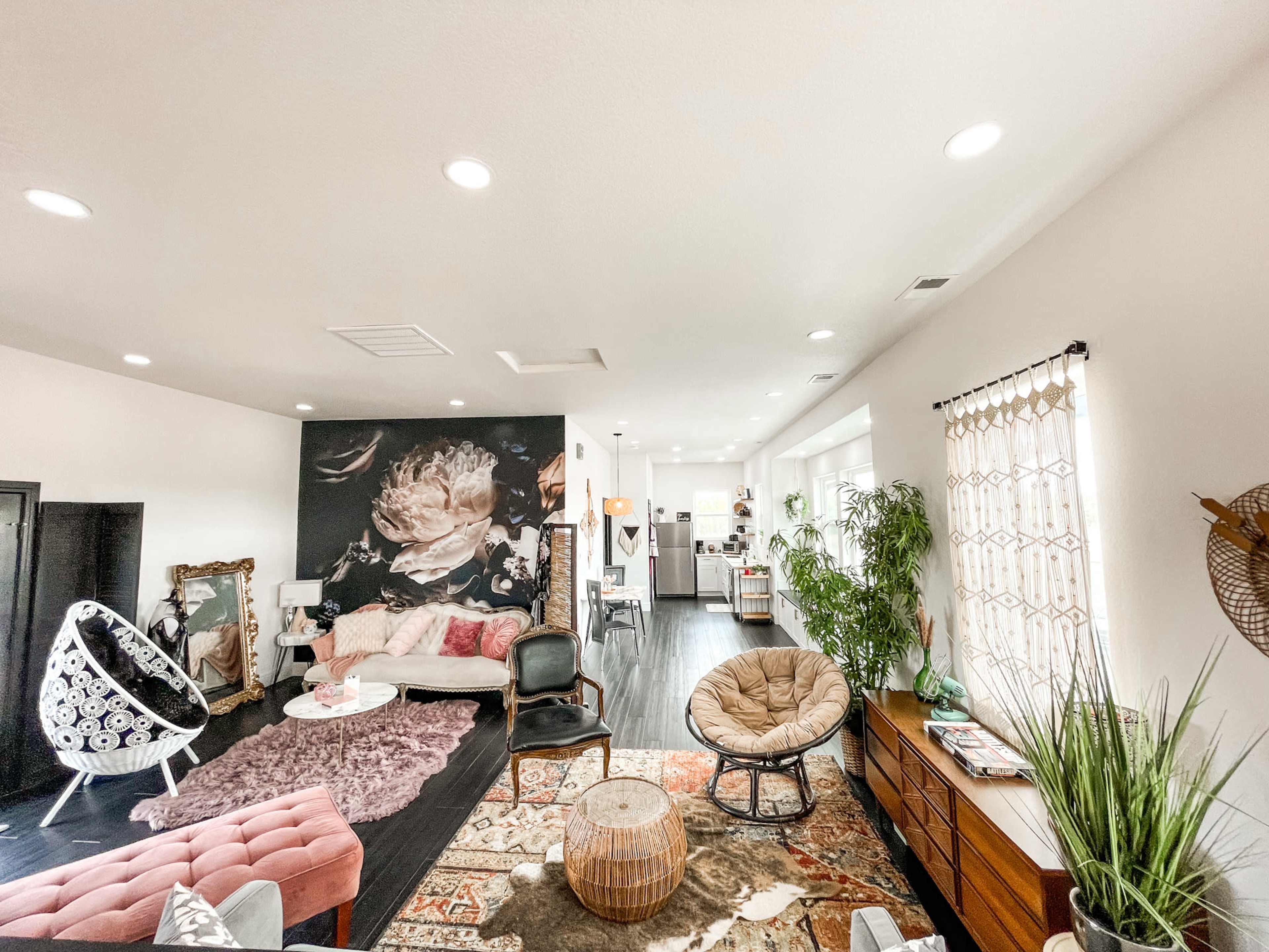 A bright, open living space featuring modern furniture, a large wall mural of a flower, and a cozy seating arrangement.