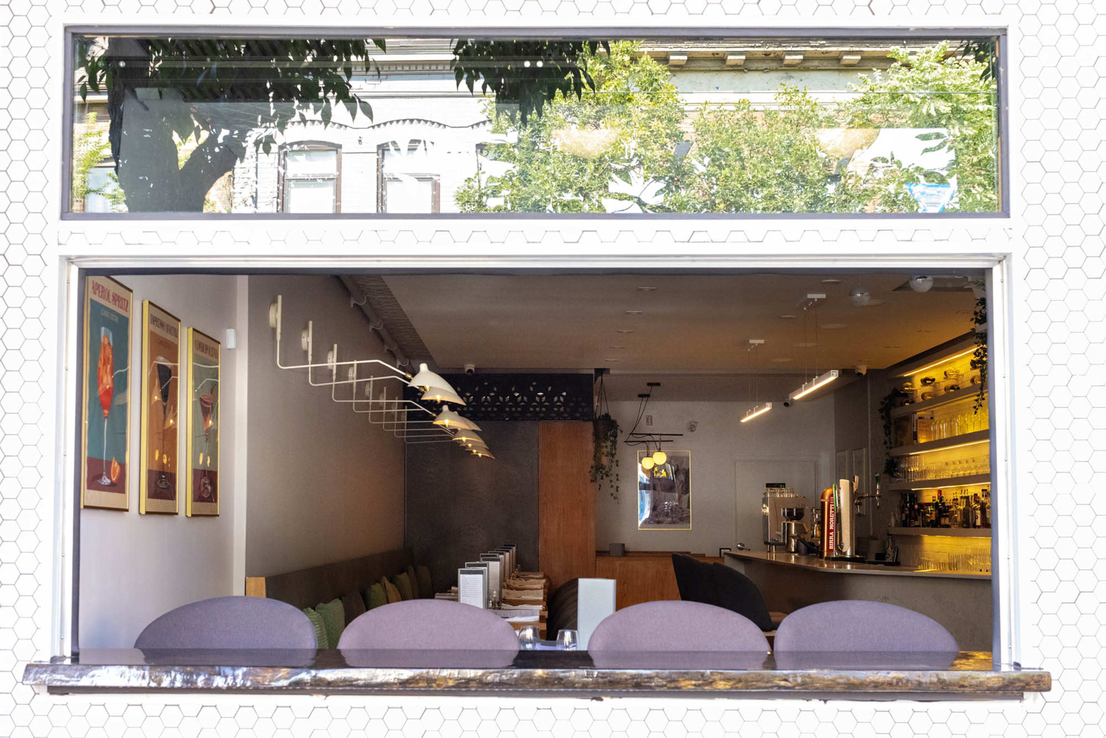 The image shows the interior of a cafe as seen through a window, featuring wall art, seating, and a bar area.