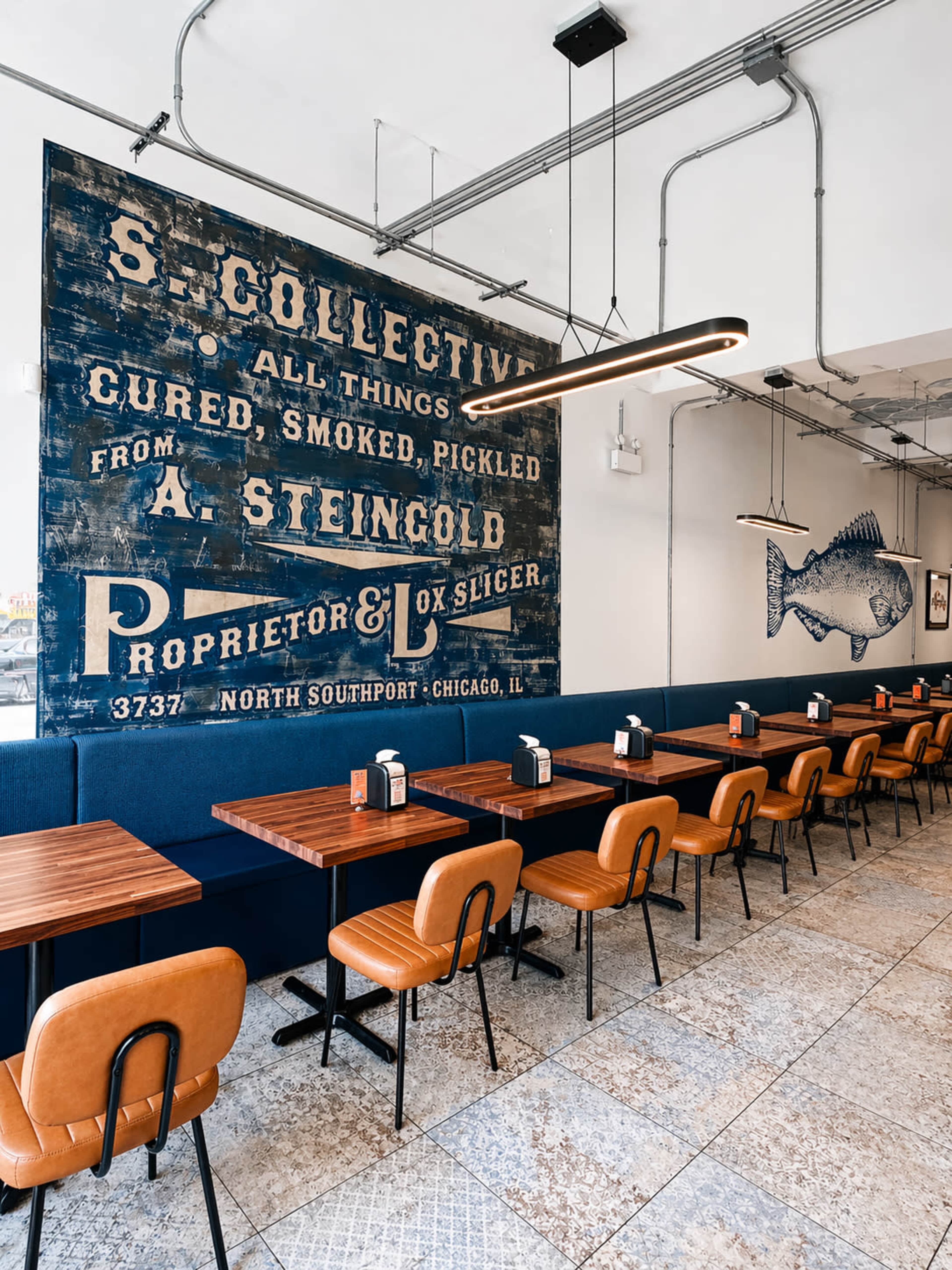 The image shows a sleek, modern restaurant interior with wooden tables, leather chairs, and a large vintage advertisement mural on one wall.