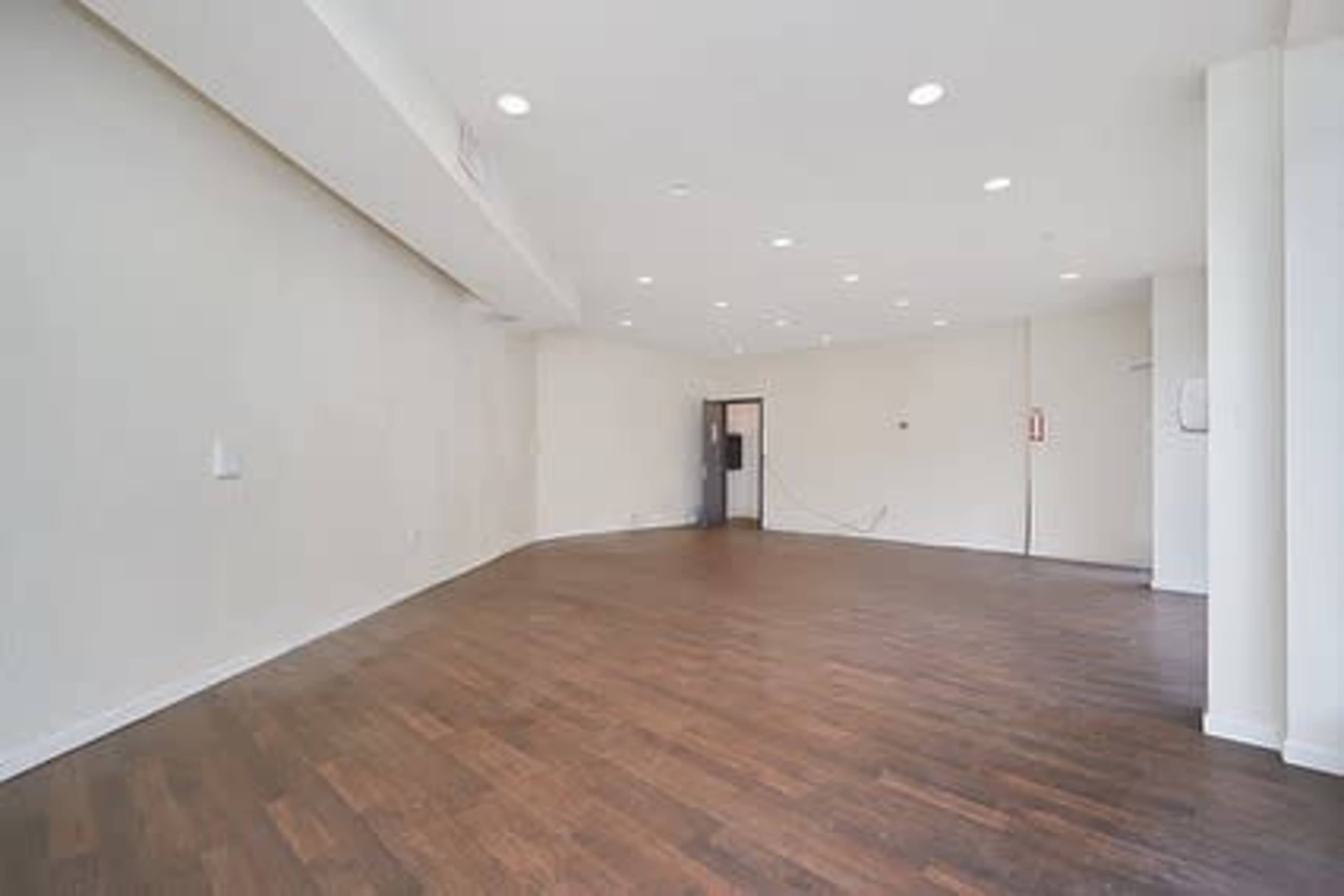 A spacious, empty room with wooden flooring and bright overhead lighting.