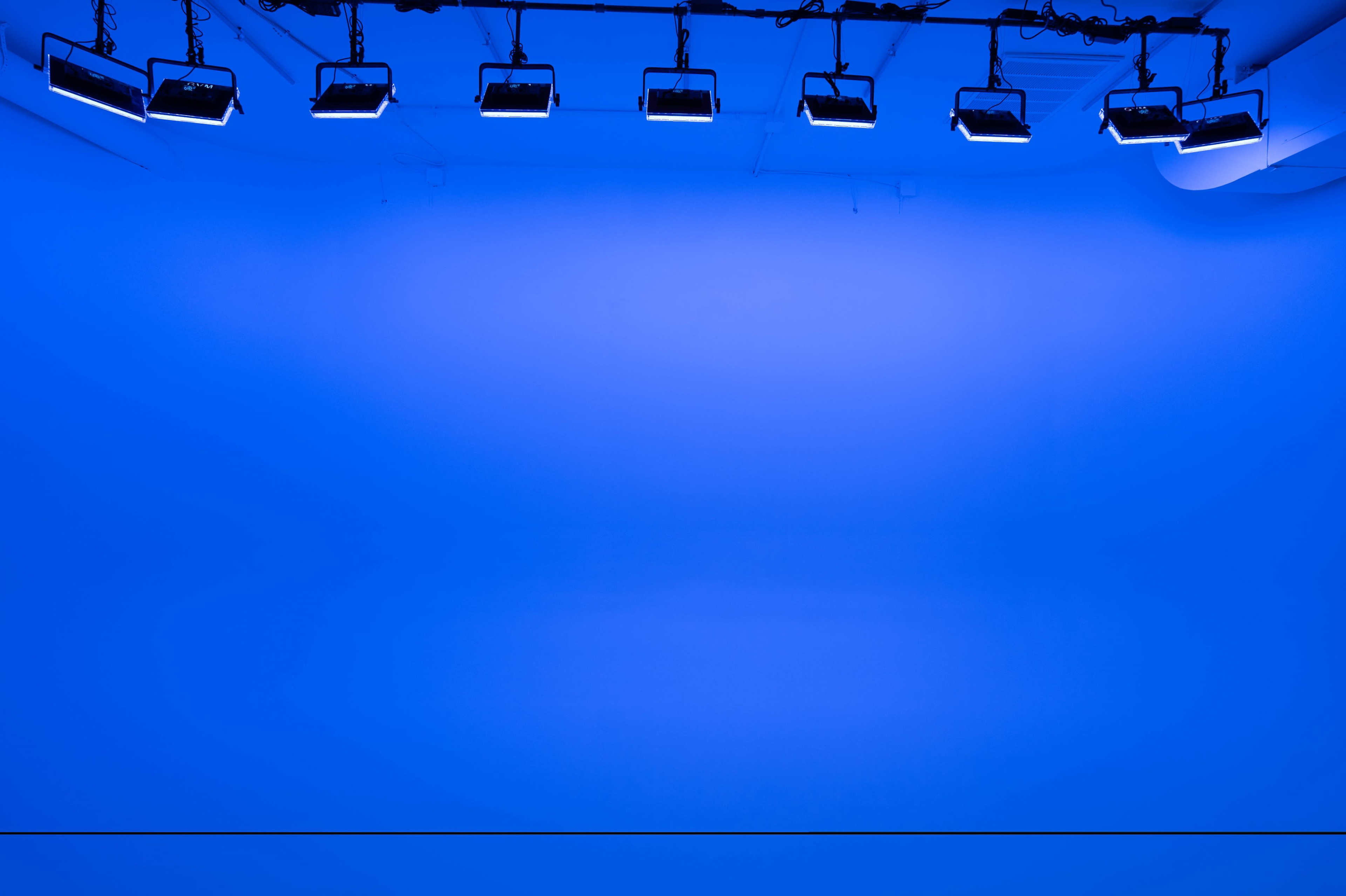 The image features a plain blue backdrop illuminated by multiple overhead lights.