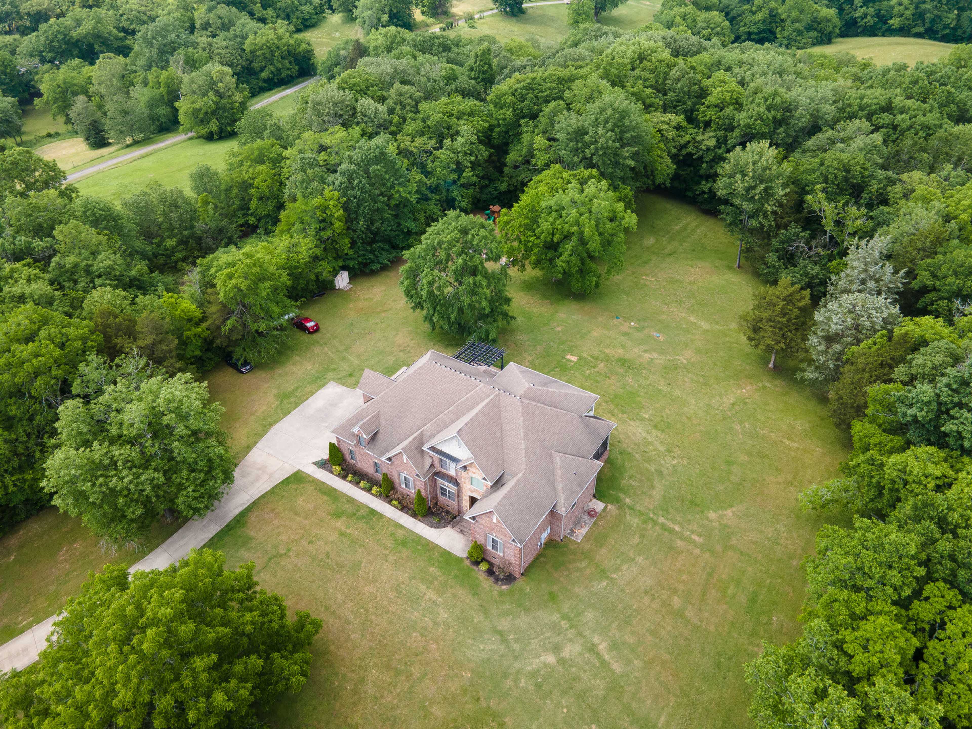 An aerial view of a large brick house surrounded by a green lawn and dense trees.