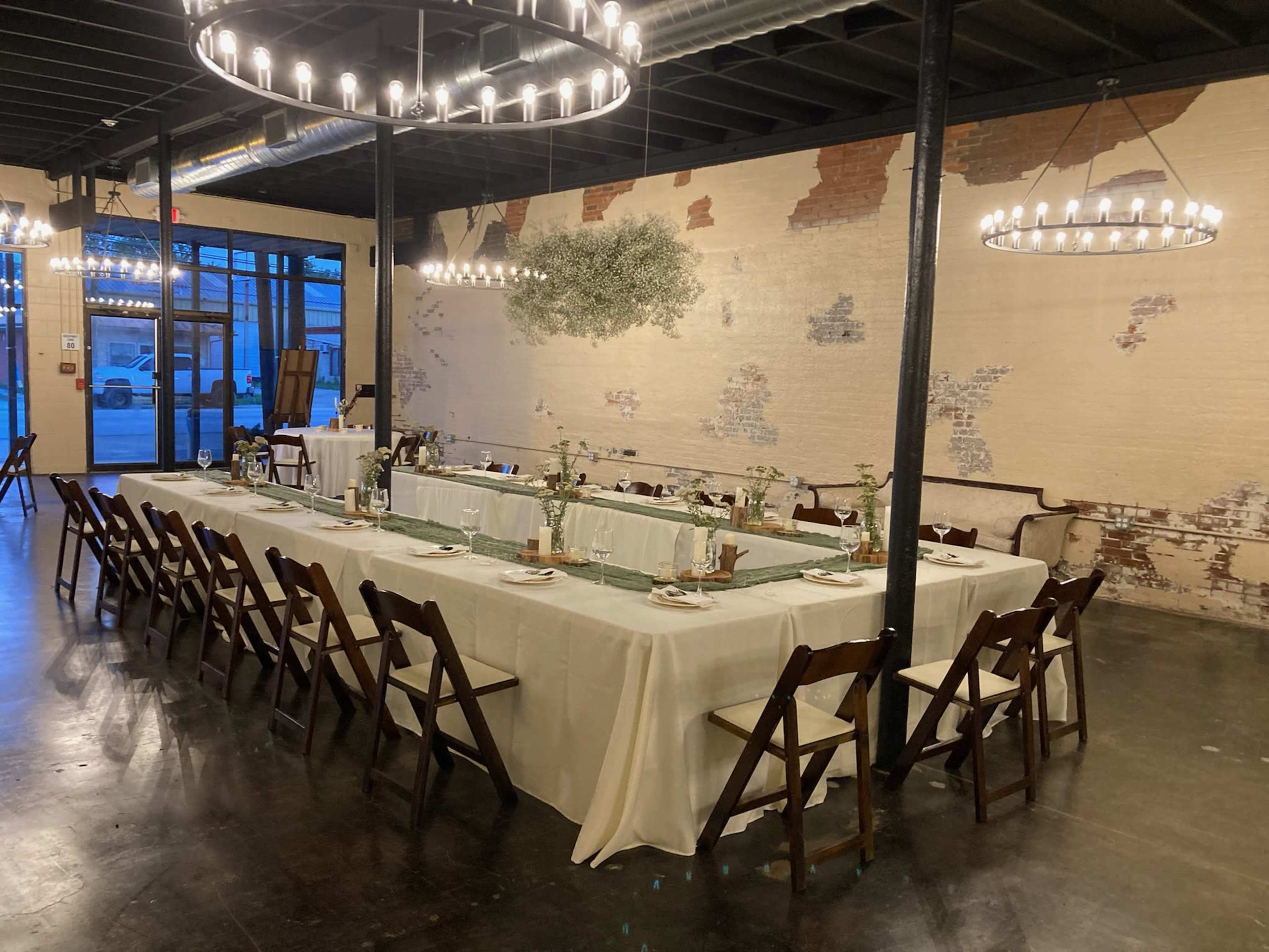 A long dining table is set for a meal in a venue with exposed brick walls and modern lighting fixtures.