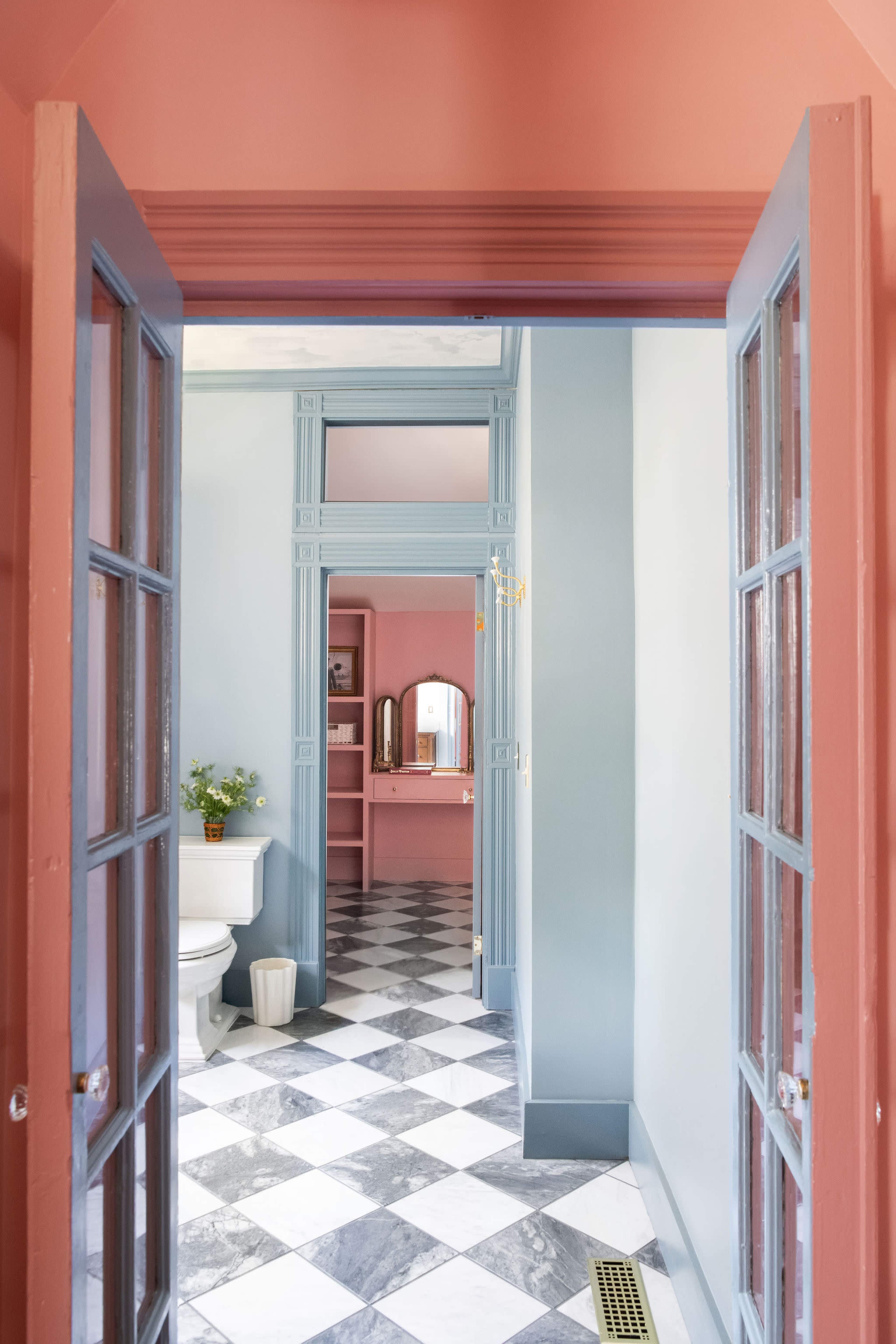 The image shows a view through an open doorway into a hallway featuring a bathroom with a checkered floor and pastel-colored walls.