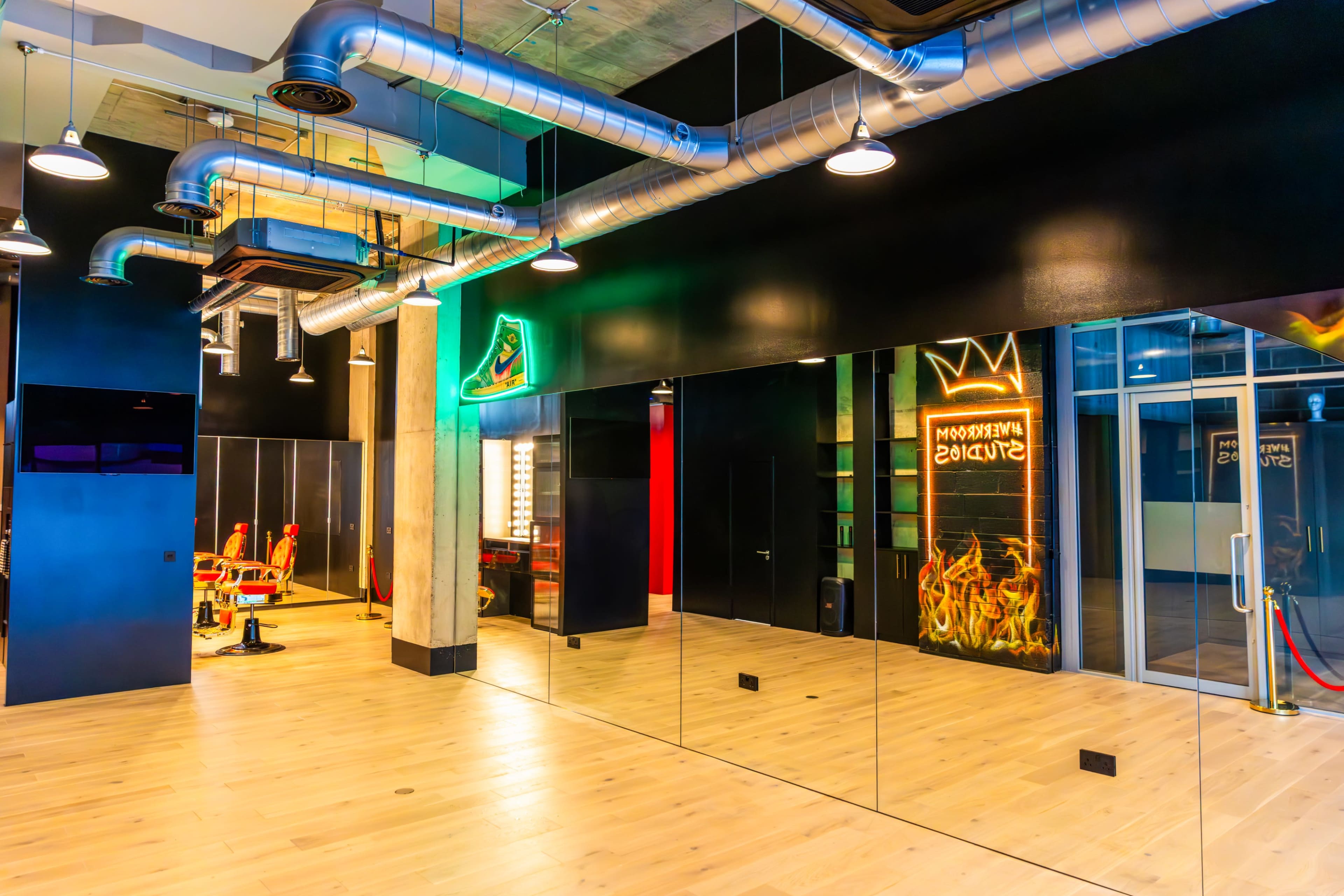 The image shows a modern studio space with large mirrors, wood flooring, and industrial-style metal ventilation.