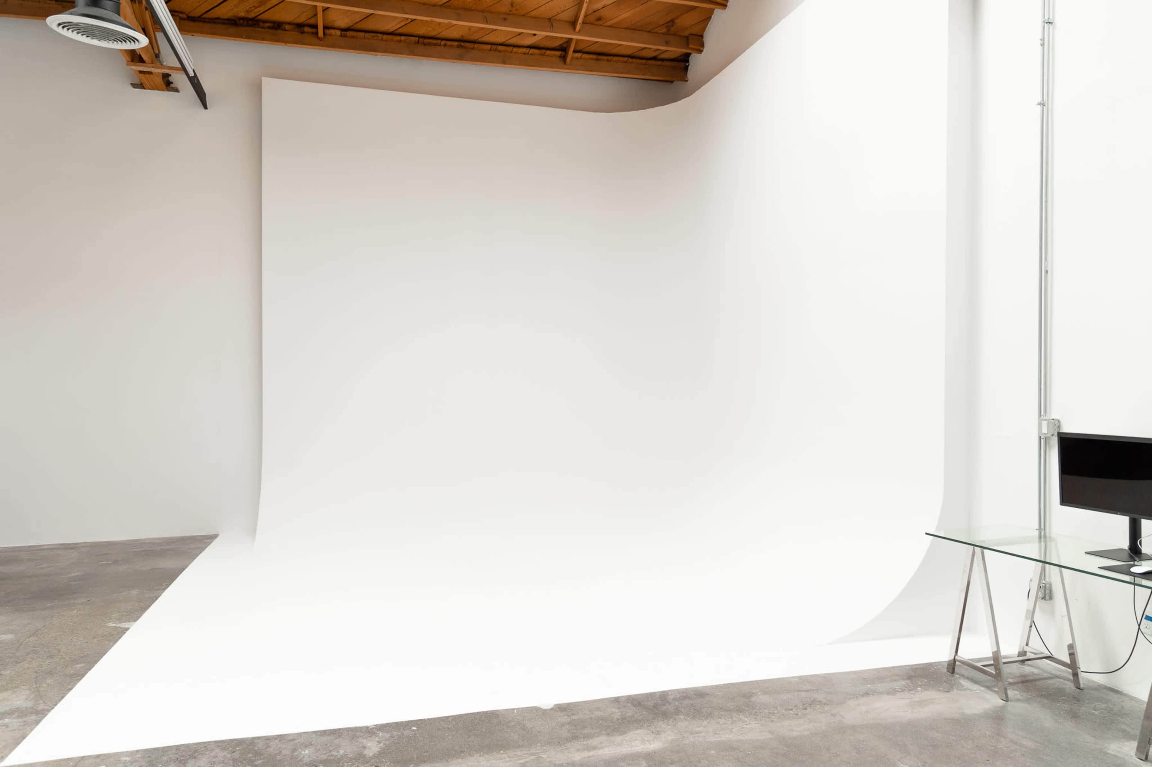 A minimalist studio space with a large white seamless backdrop and a glass table in the corner.