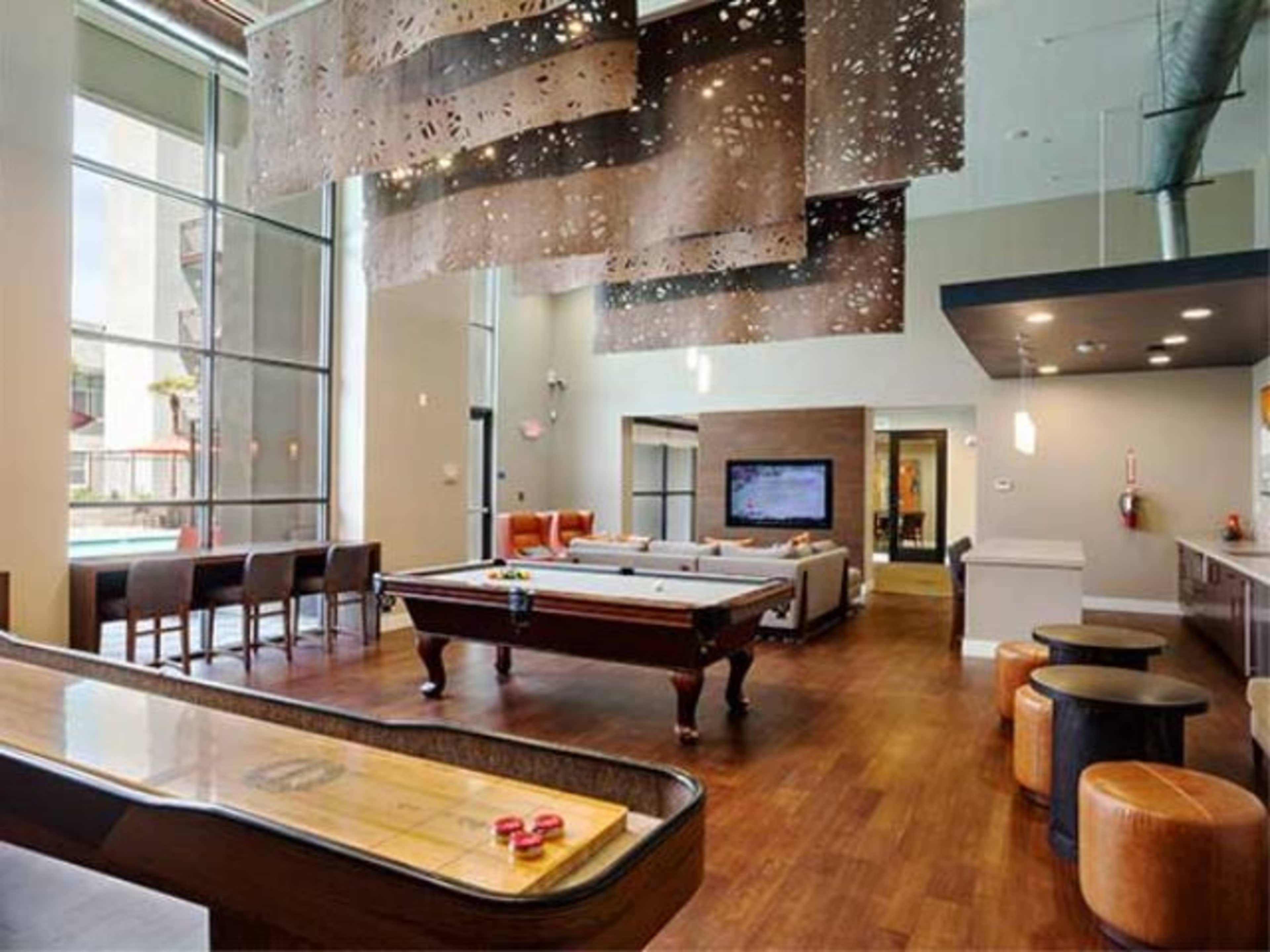 A spacious indoor recreation area featuring a pool table, shuffleboard, and a large television, with modern furniture and large windows.