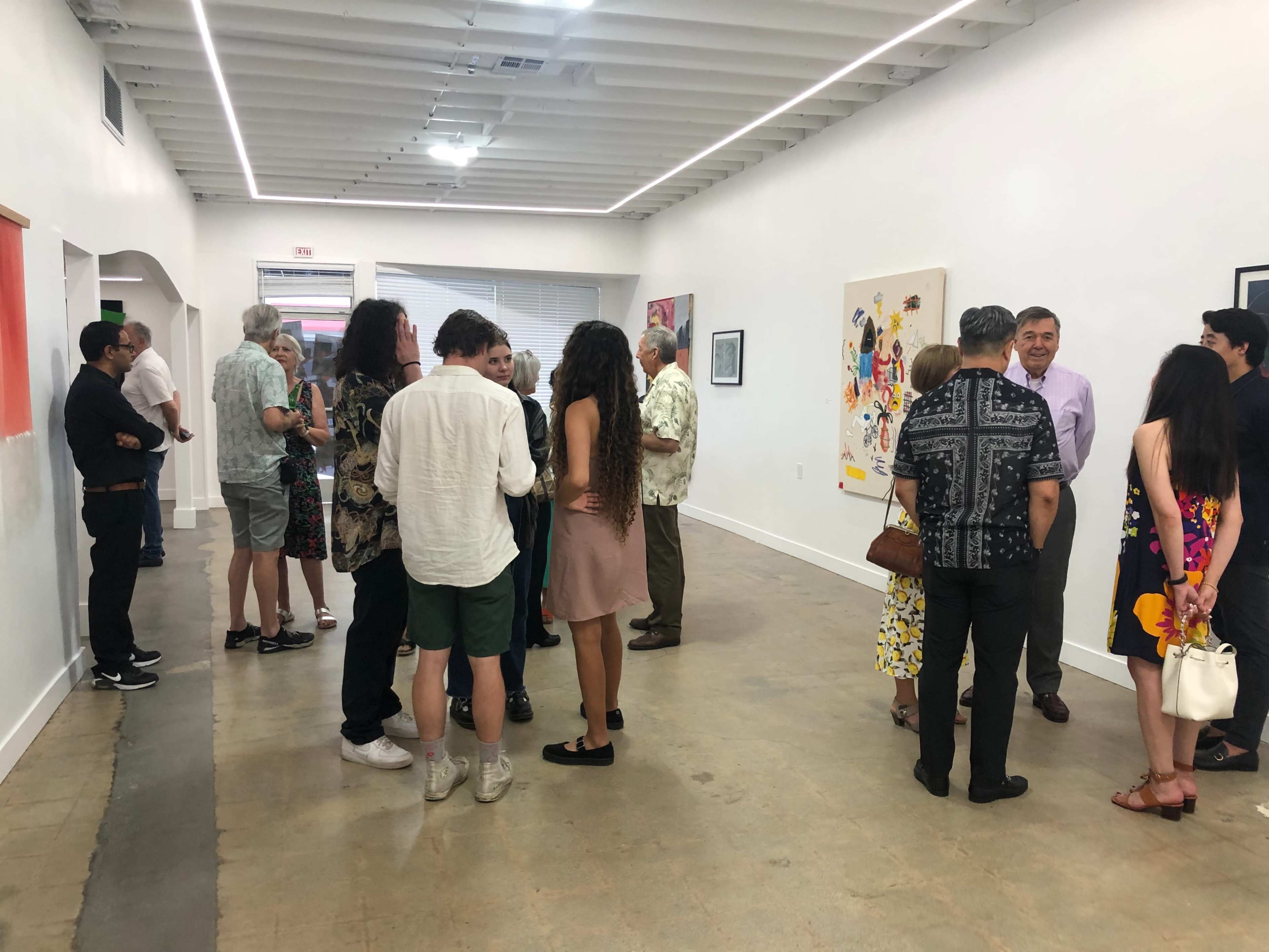 A group of diverse individuals gathers in an art gallery, engaging in conversation while observing various artworks displayed on the walls.