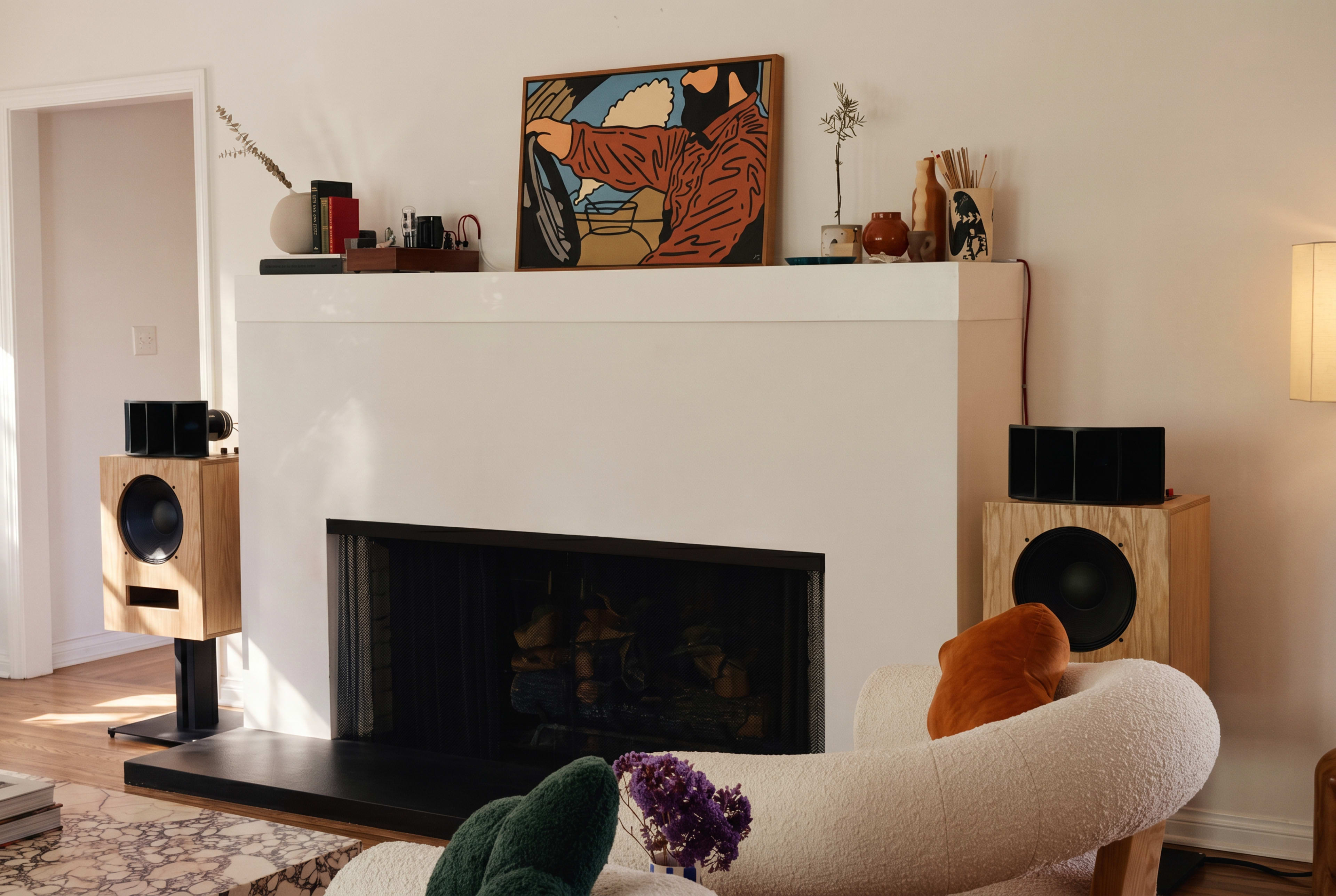 The image features a cozy living room with a modern fireplace, two speaker systems on either side, and artwork displayed above the mantel.