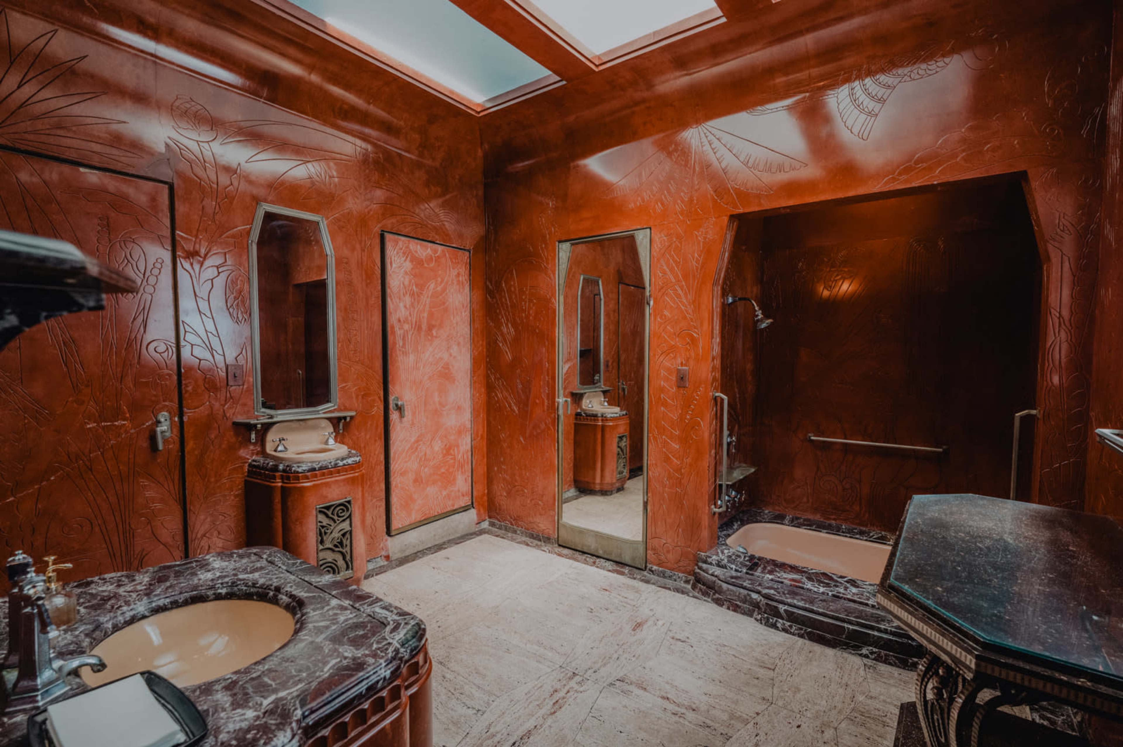 The image shows a vintage bathroom with red marbled walls, multiple mirrors, and dark stone countertops.