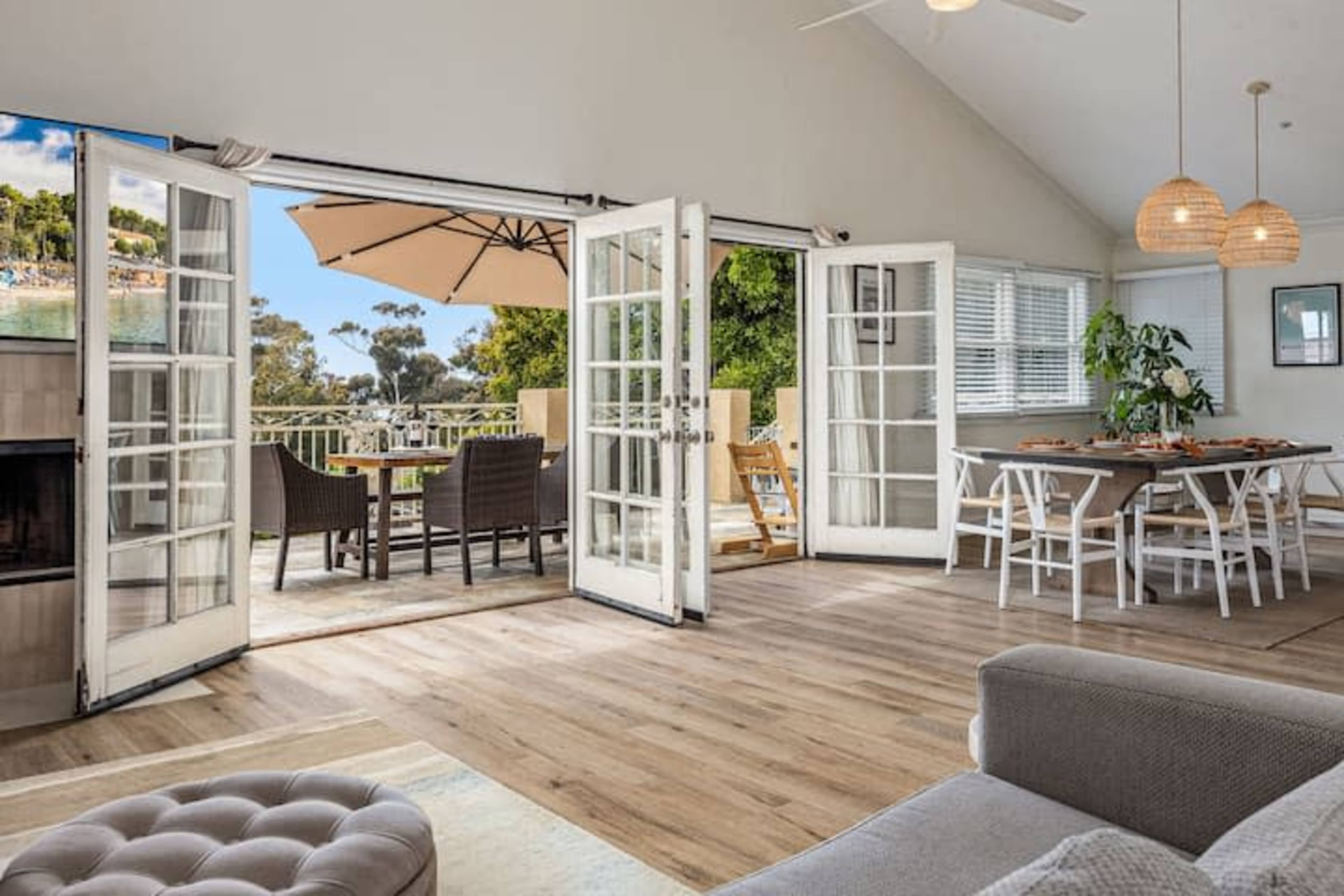 The image shows a bright, open living space with French doors leading to an outdoor dining area and a modern interior featuring a dining table and cozy seating.