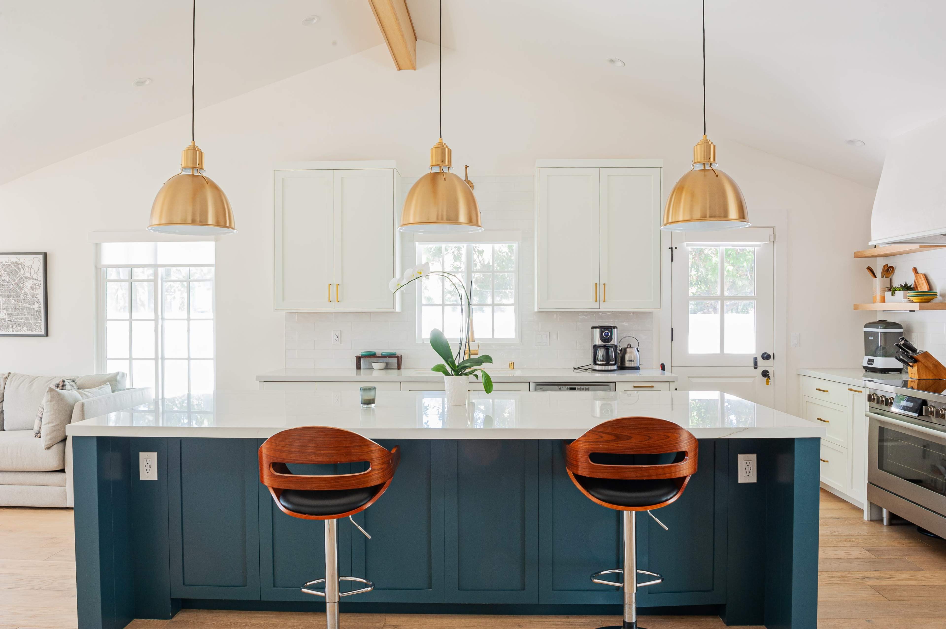 A modern kitchen features a large island with two bar chairs, white cabinetry, and three pendant lights overhead.