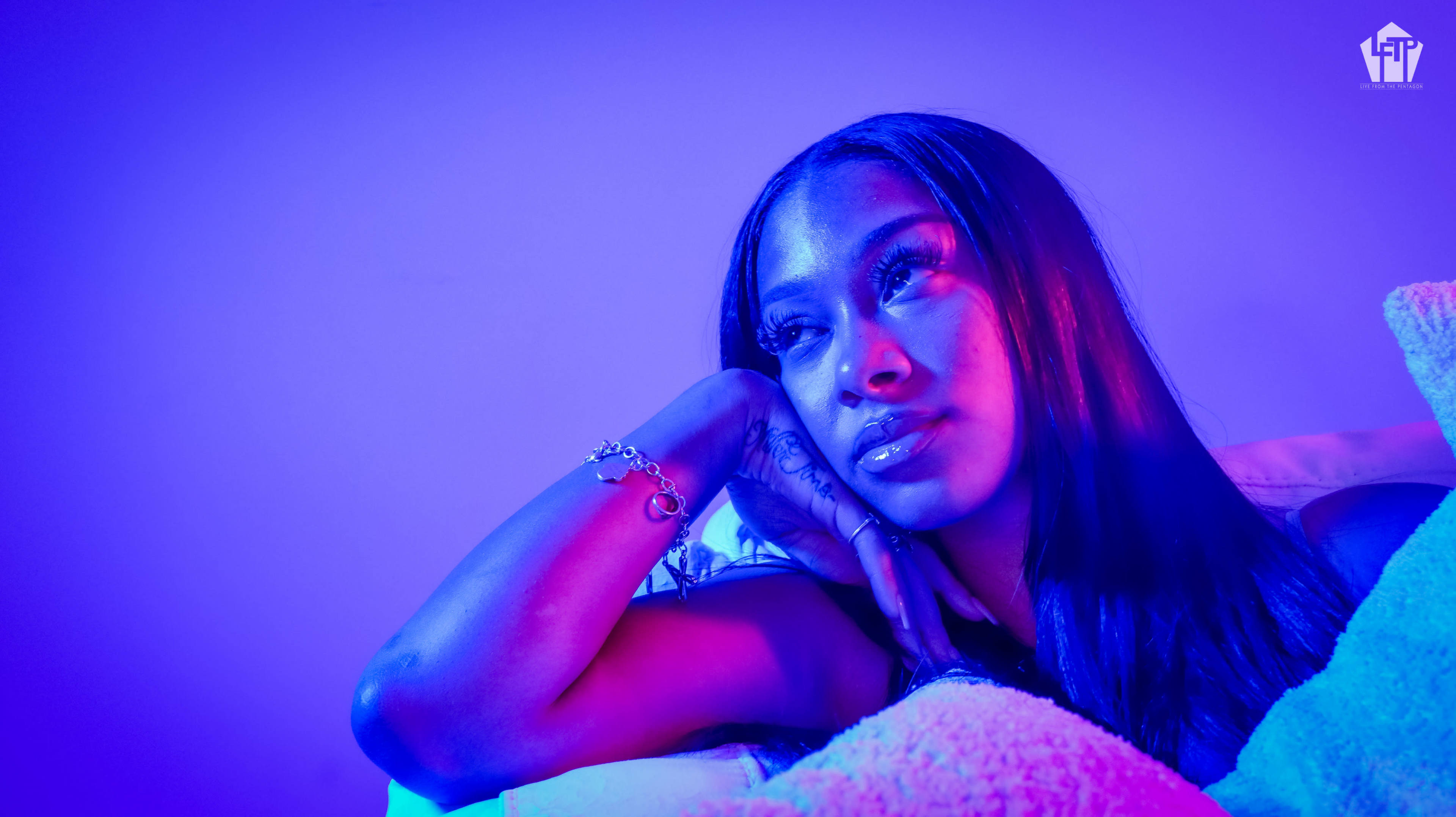 A person rests their head on their hand while lying down, surrounded by soft lighting that casts a blue and purple hue on the scene.