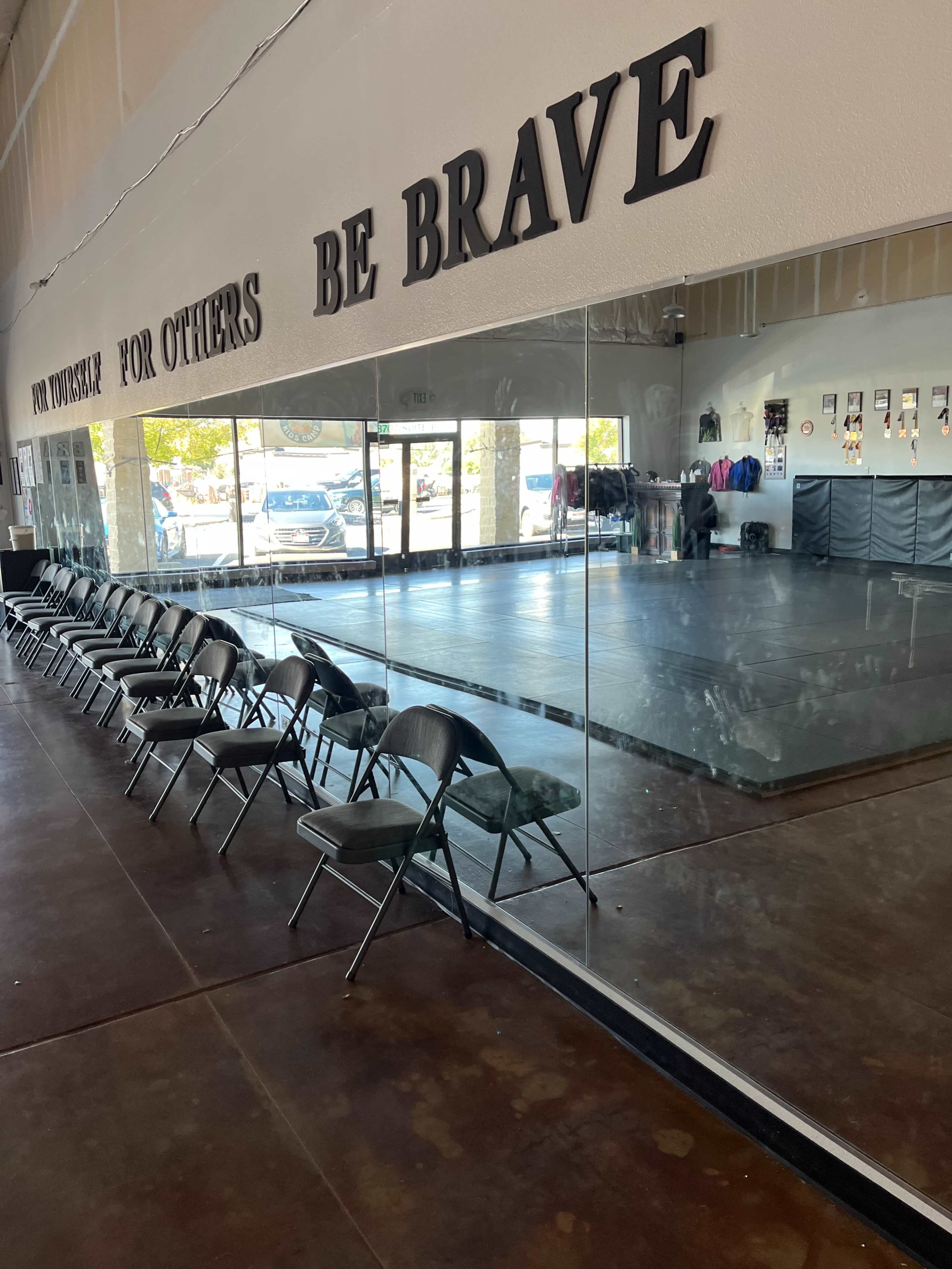 The image shows a dance studio with a mirrored wall, empty chairs lined up against one side, and visible reflections of the interior space.