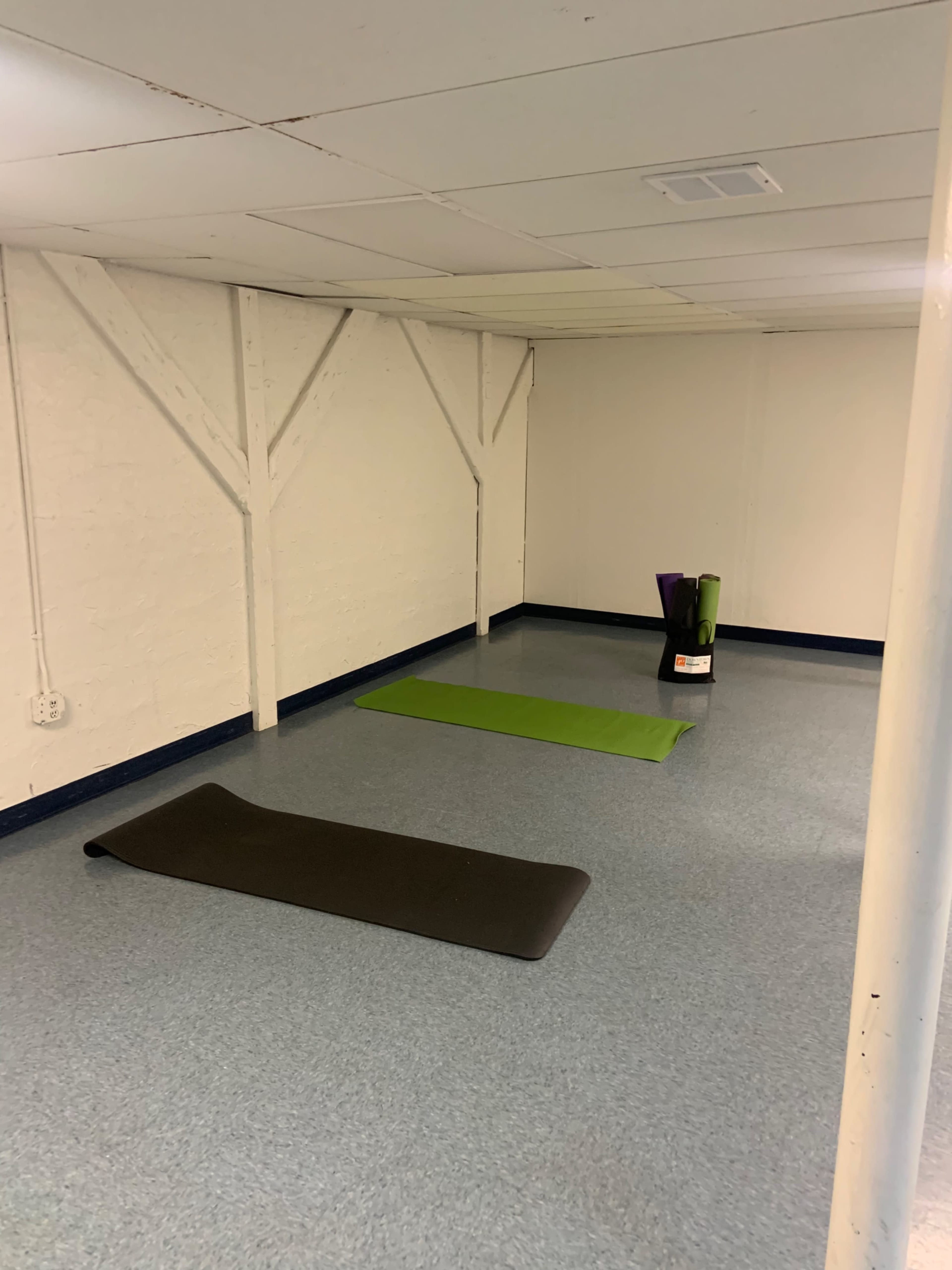A sparsely furnished room with two yoga mats on the floor and a container of yoga props in one corner.