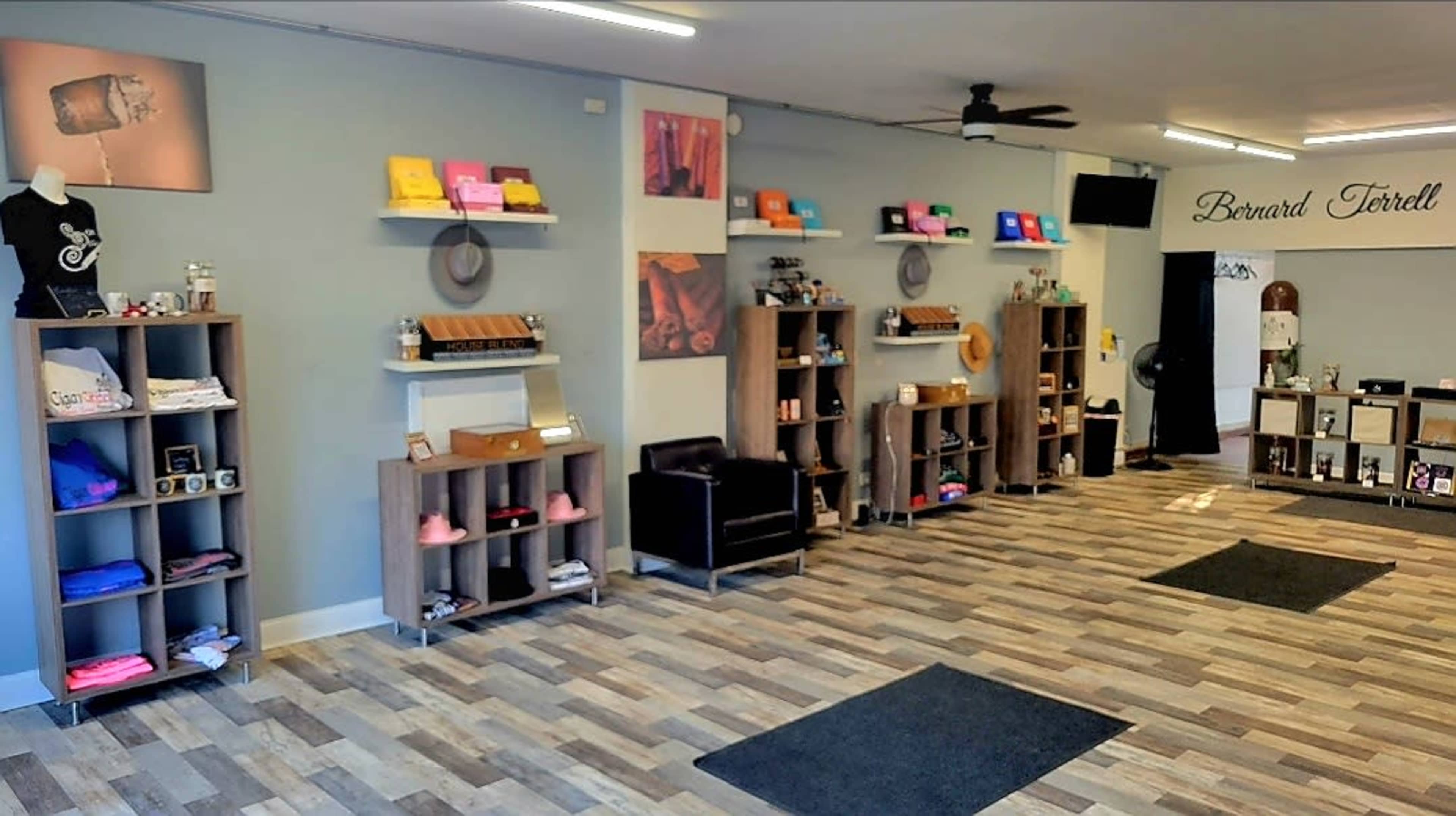 The image shows an interior retail space with shelves displaying various products, including clothing and accessories, arranged neatly along the walls, and a seating area in the corner.