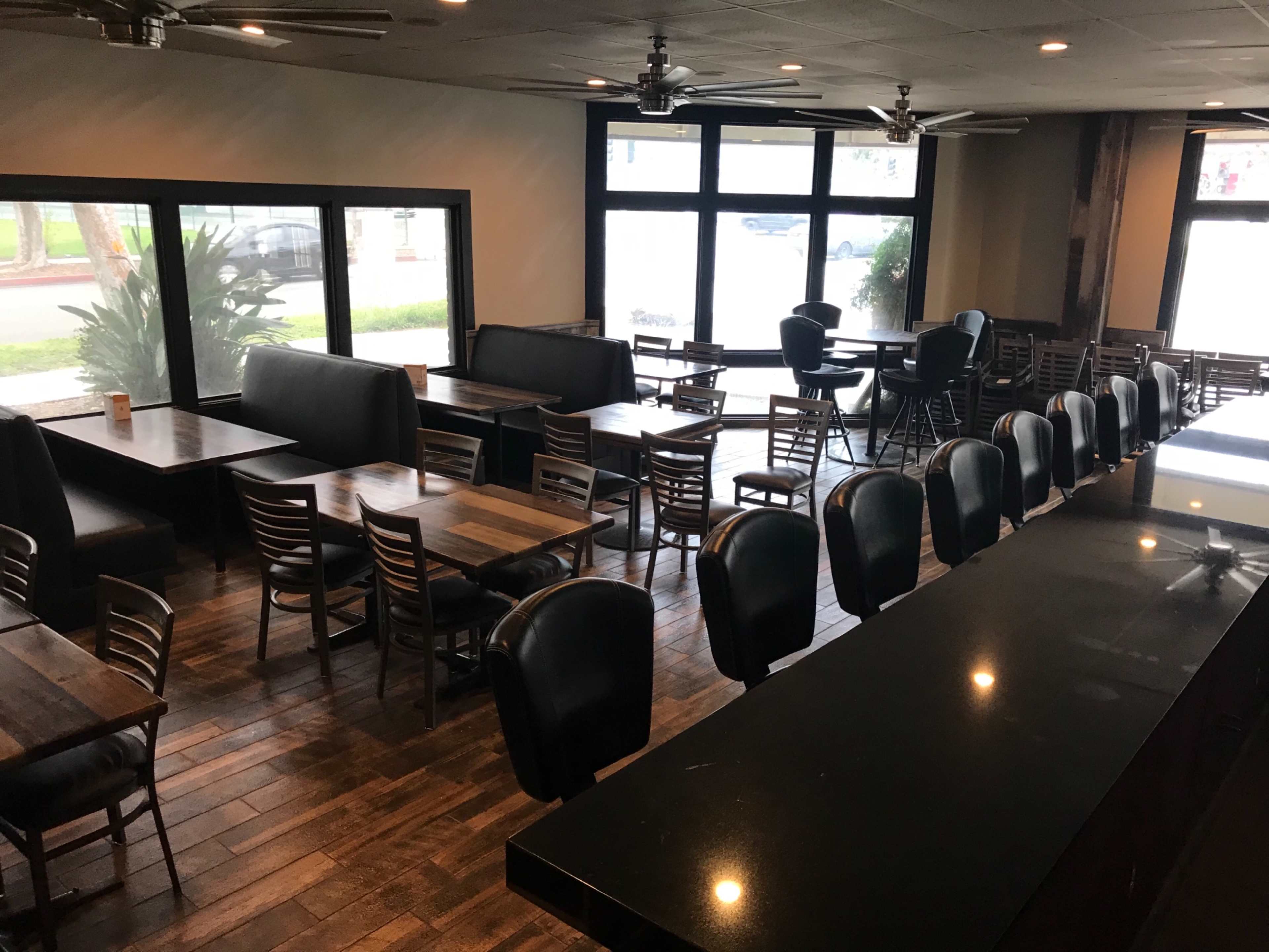 A spacious restaurant interior featuring dark wood tables, leather chairs, and large windows that provide natural light.