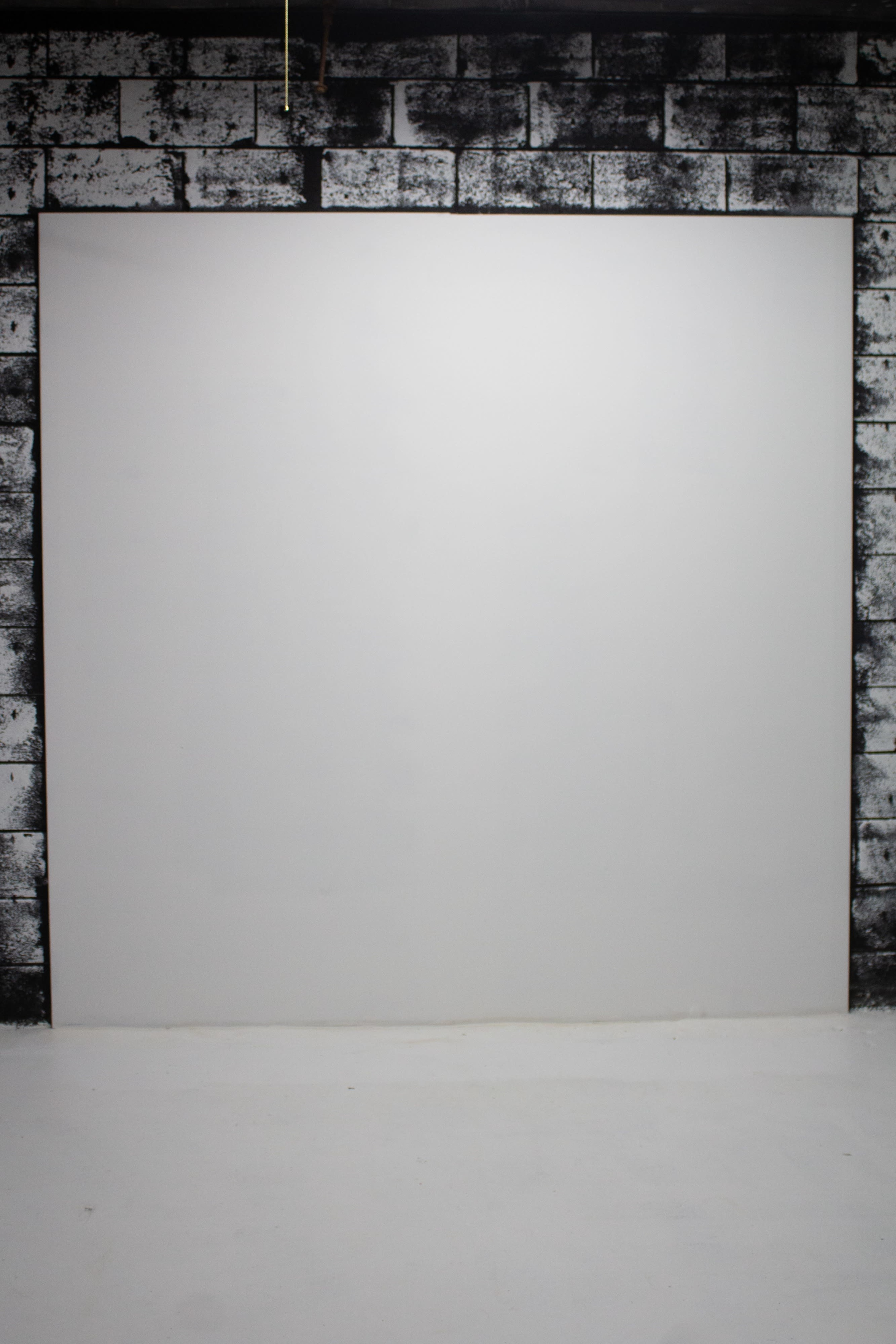 A large blank white canvas is mounted on a wall with a textured, black-and-white patterned surface.