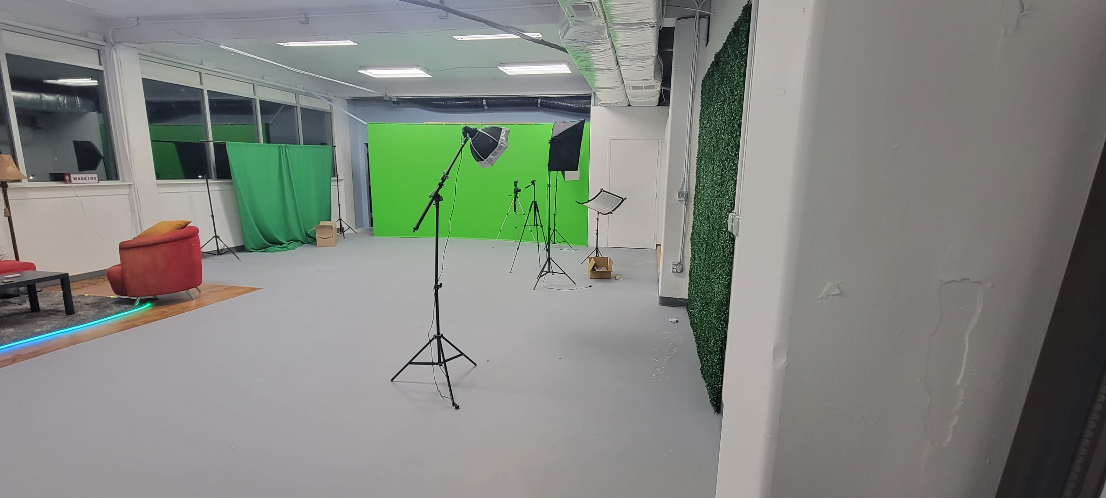 A photography studio with green screens, tripods, and a red chair in a well-lit space.