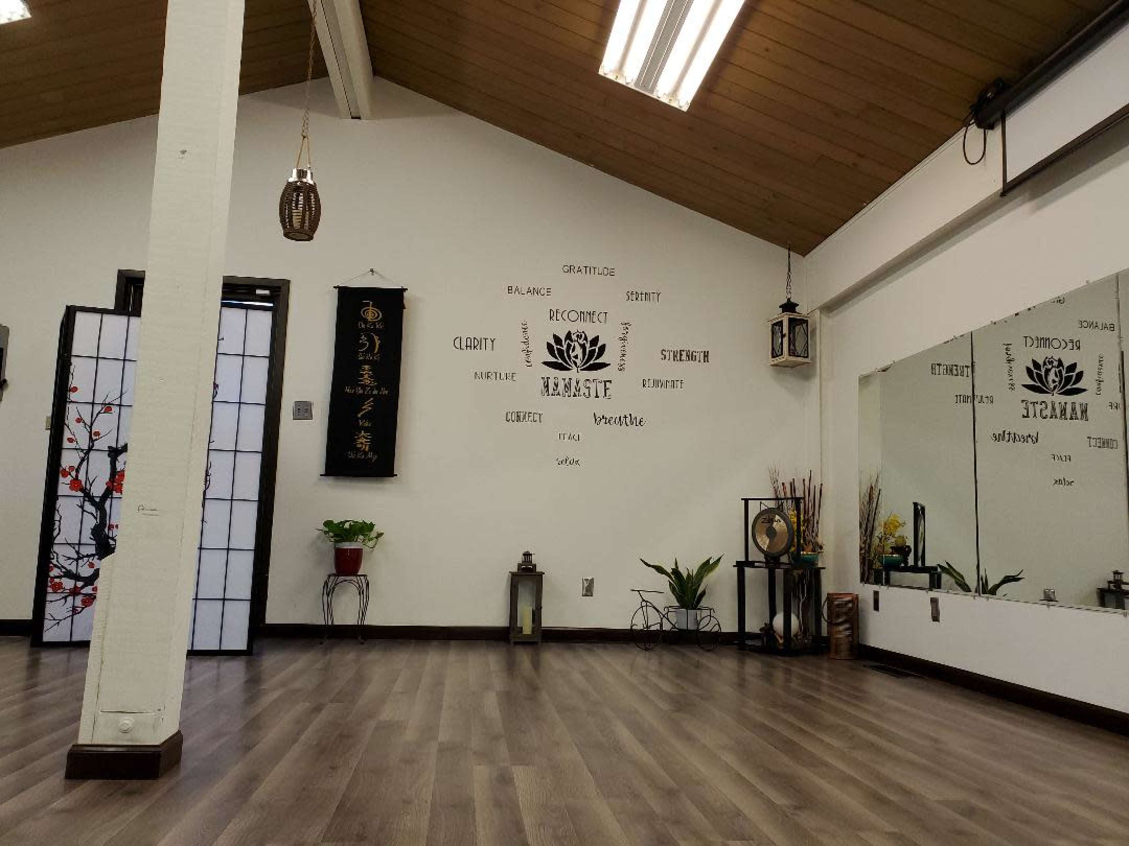 A minimalist interior of a yoga or meditation studio featuring wooden flooring, wall decorations with motivational words, and a large mirror.
