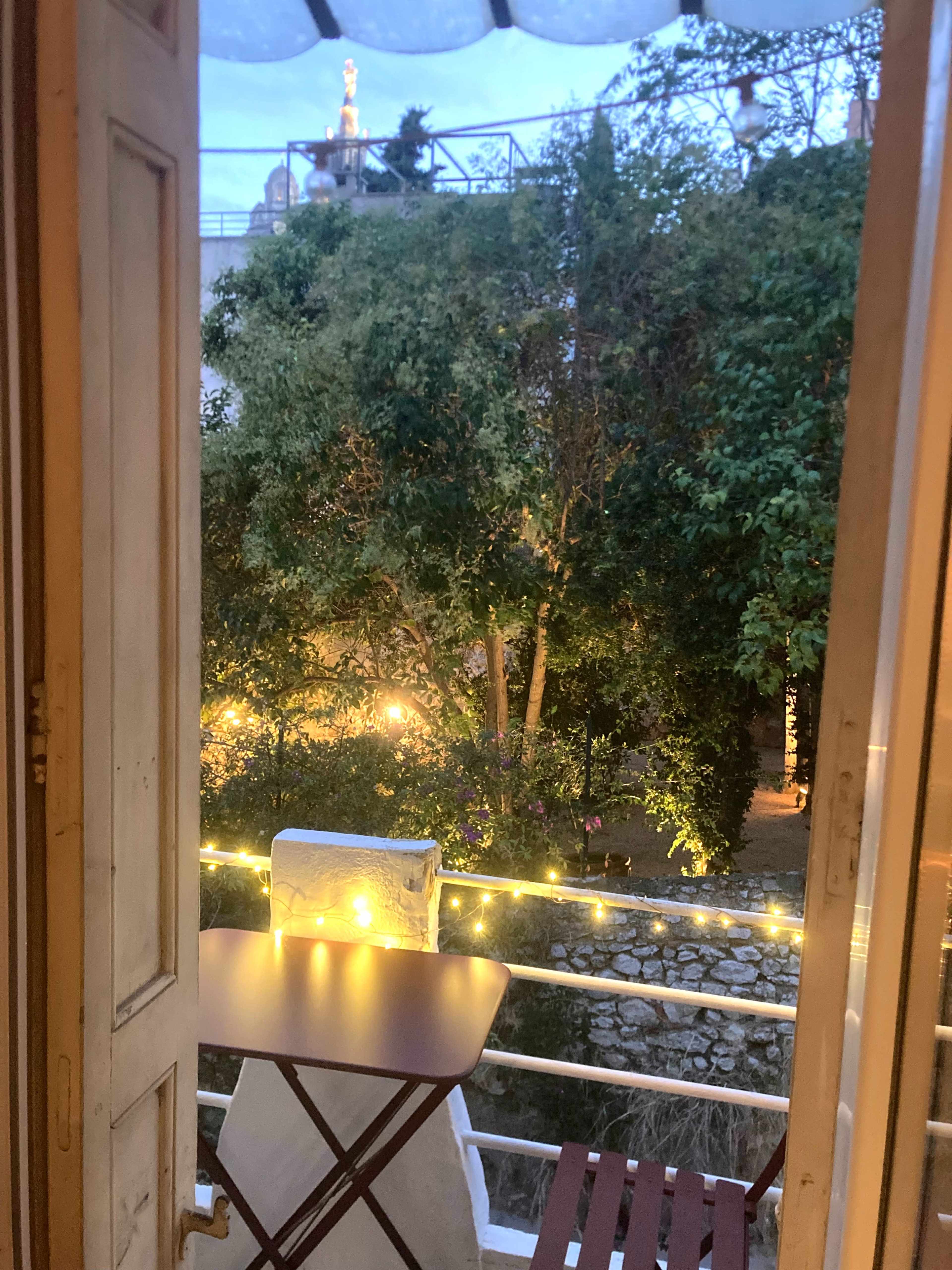 The image shows a view from a doorway overlooking a garden illuminated by soft lights, with trees and a stone wall visible in the background.