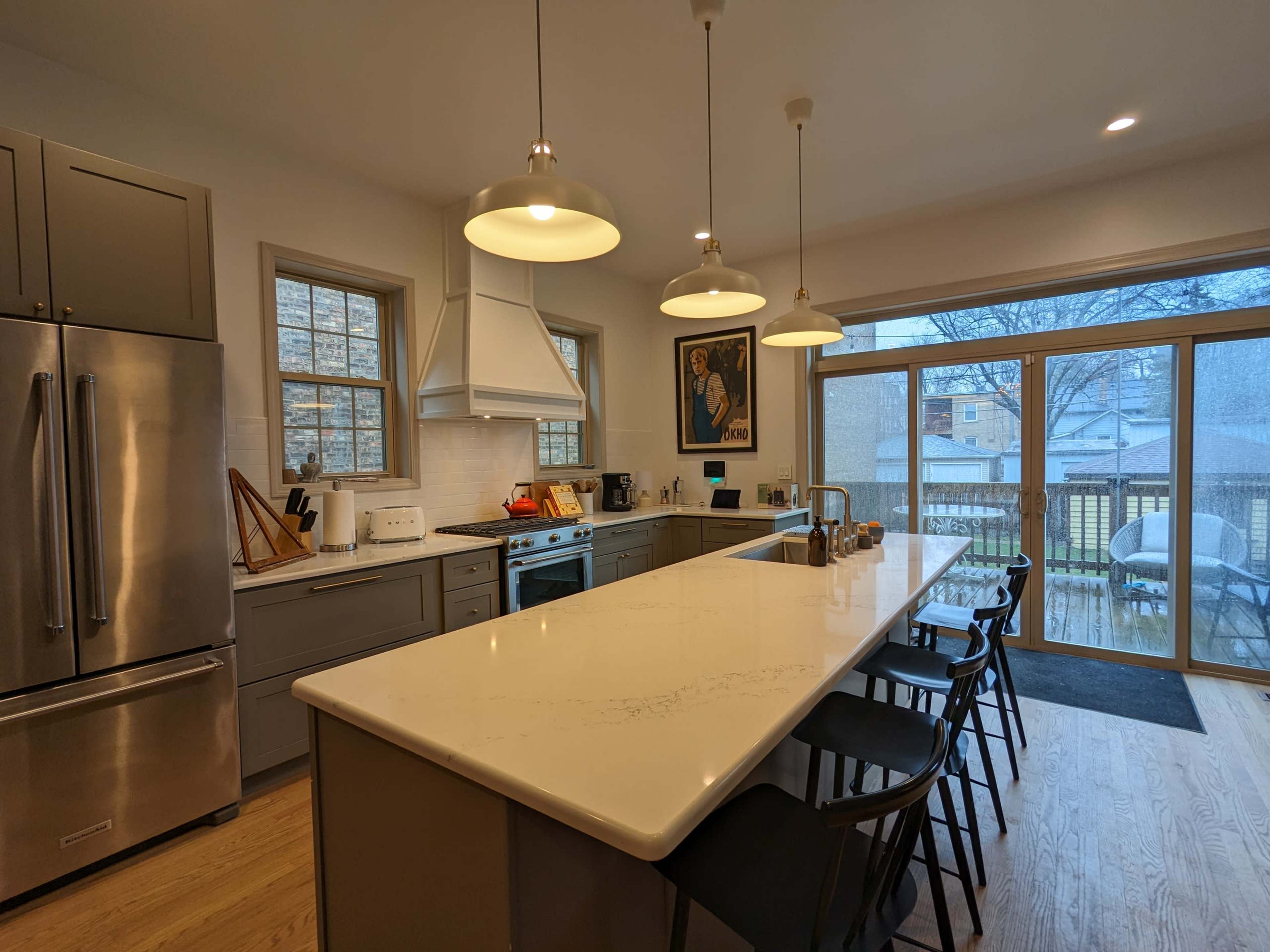 A modern kitchen features a large island with bar stools, stainless steel appliances, and large windows overlooking a snowy outdoor scene.