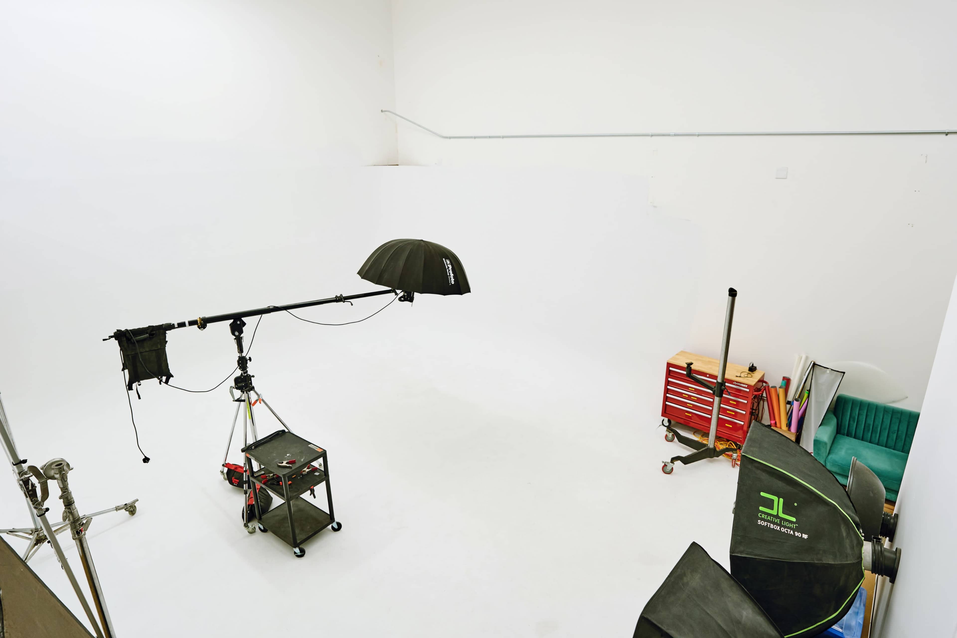 The image shows a spacious, white photography studio equipped with lighting equipment and a cart holding various tools and materials.