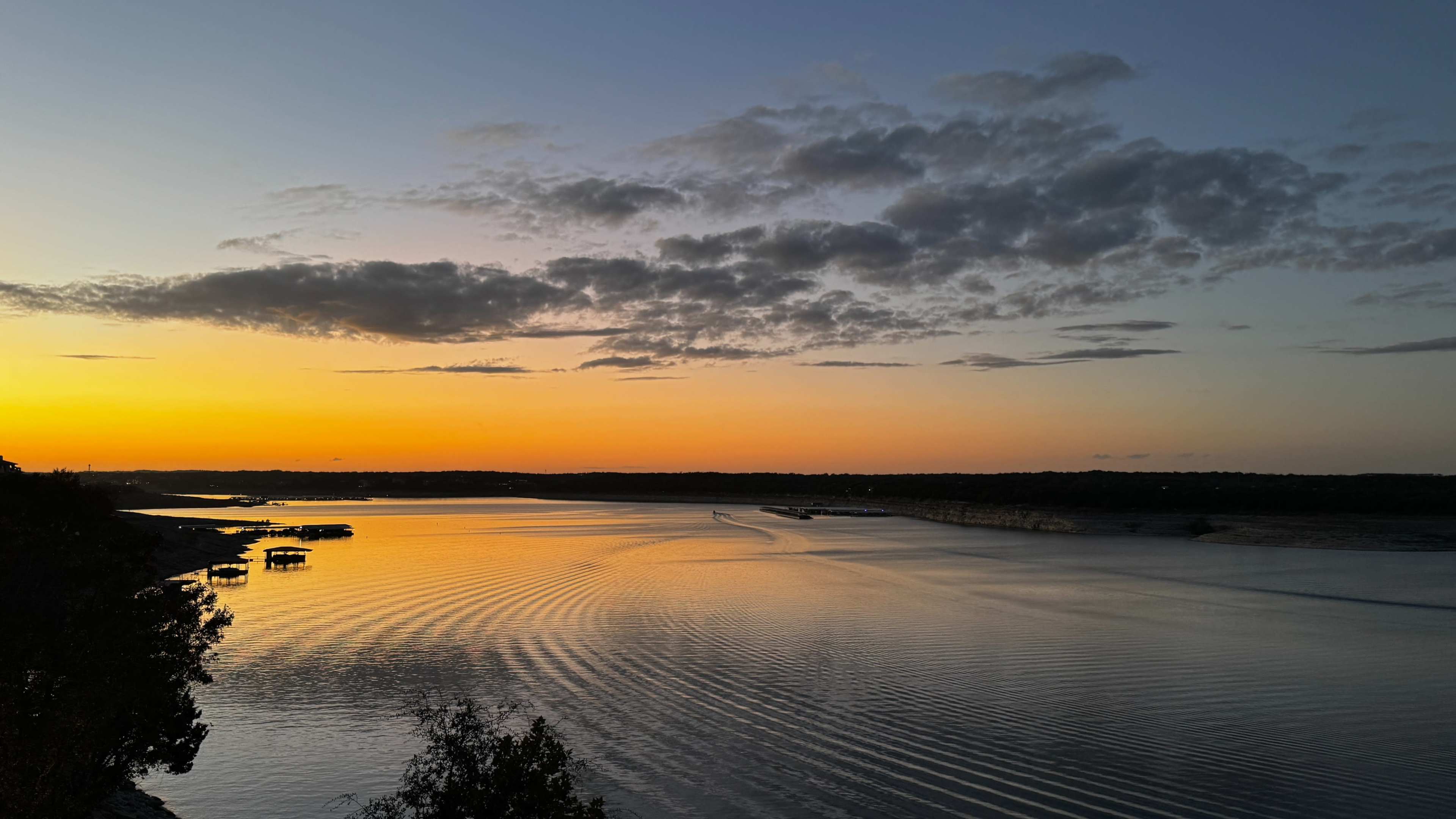 The image depicts a tranquil lake at sunset with rippling water reflecting hues of orange and purple in the sky.