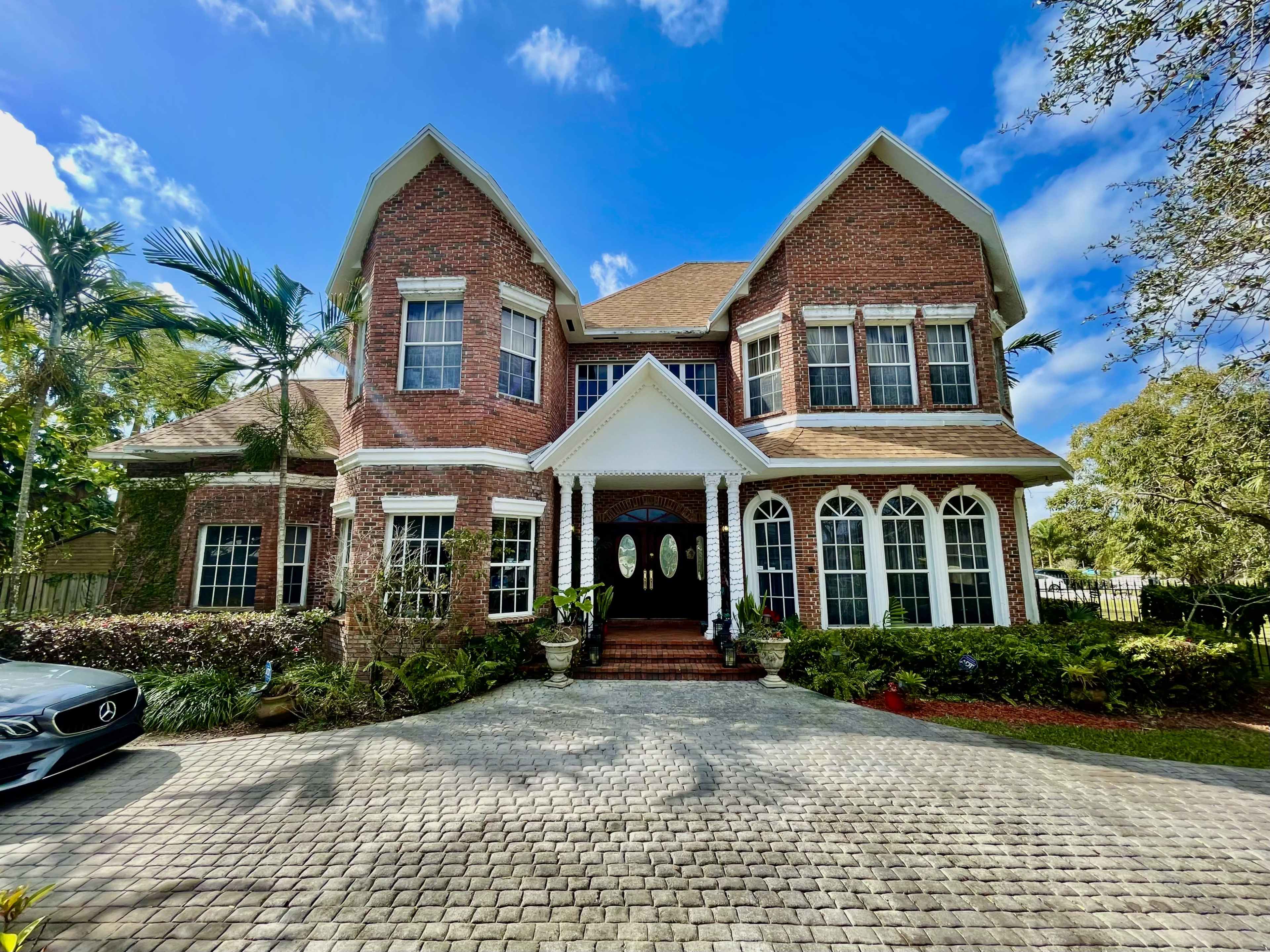 The two-story red brick house features large arched windows, a gabled roof, and a landscaped front yard with a brick driveway.
