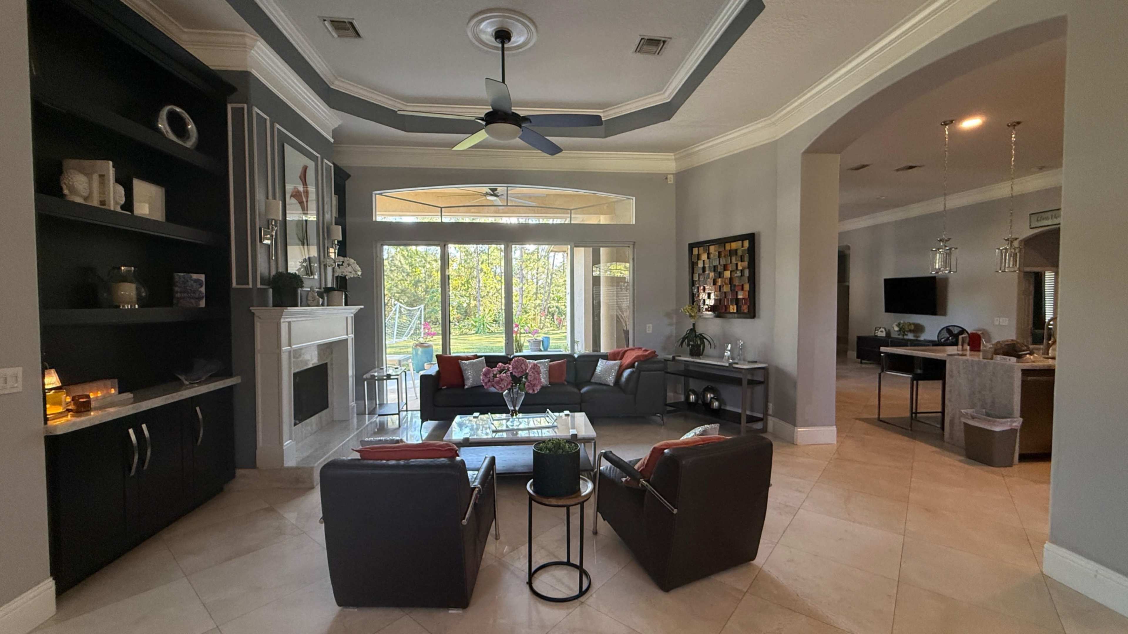A modern living room features a seating area with black leather chairs, a coffee table, and a large window showcasing a view of the outdoors.
