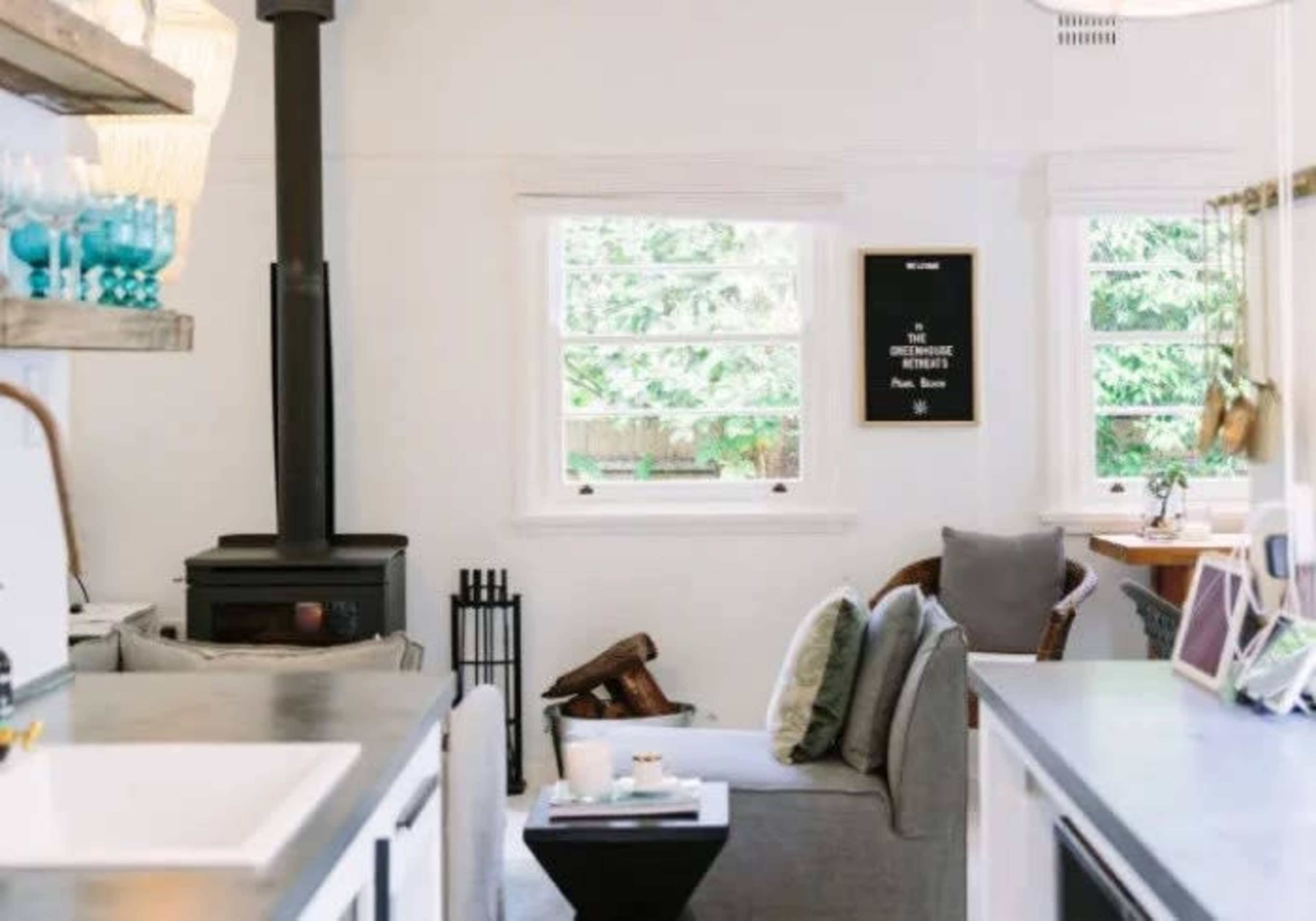 A cozy living space featuring a gray sofa, a small black side table, and a wood stove in front of a window with greenery outside.