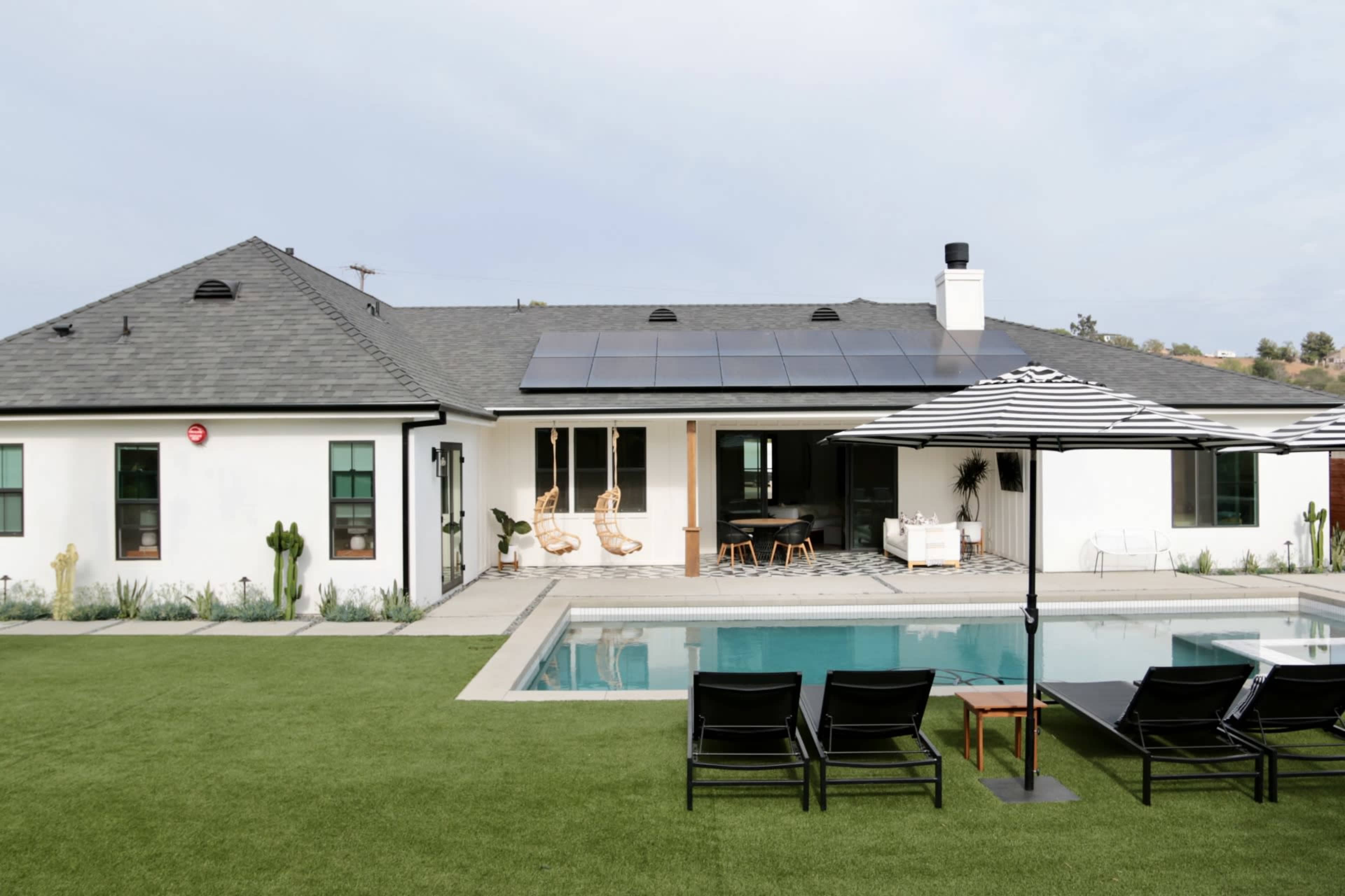 A modern single-story house with solar panels and a swimming pool is surrounded by a well-maintained lawn and lounge chairs.