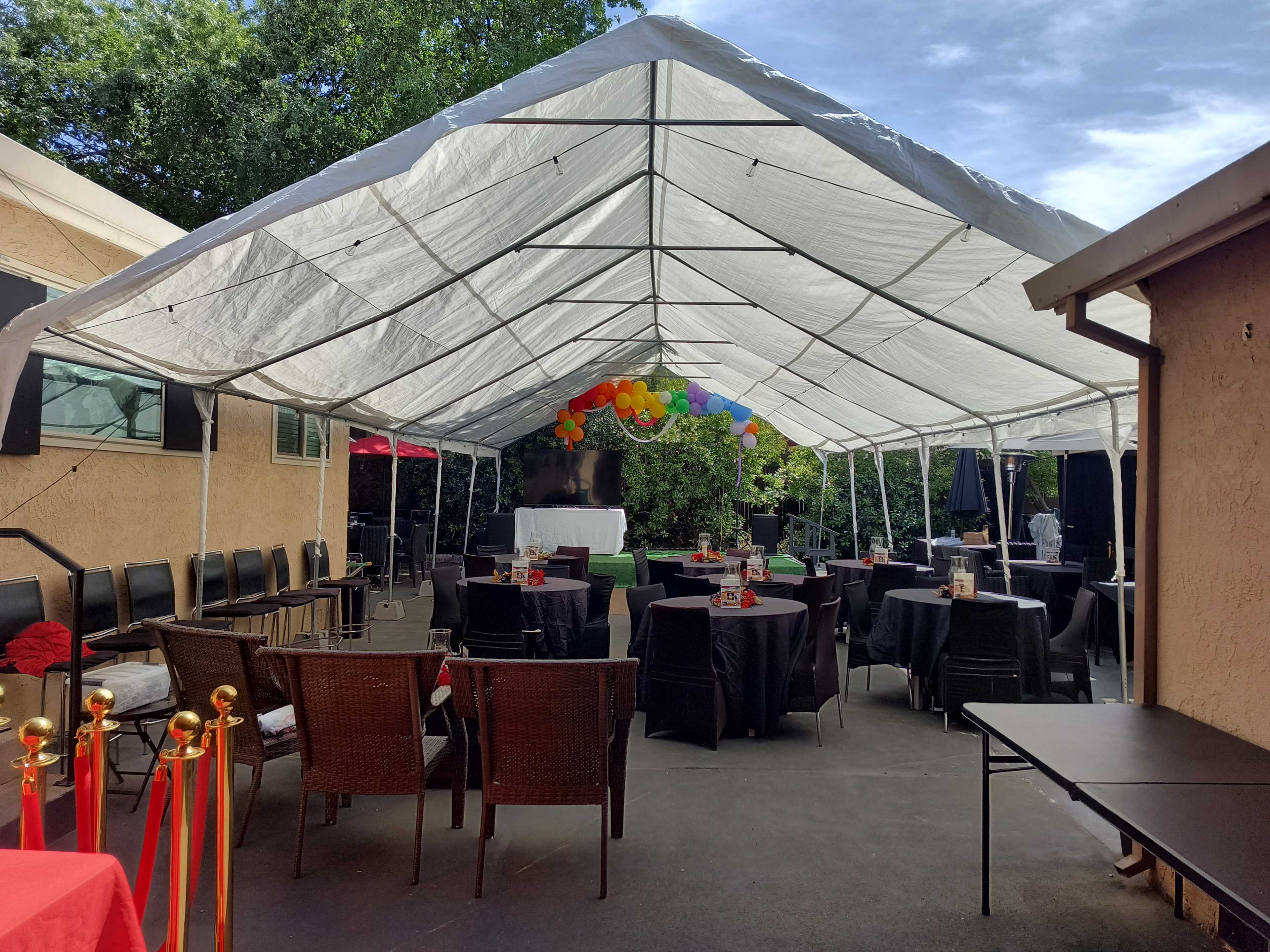 A large white tent is set up for an outdoor party, featuring tables with black and red tablecloths and colorful decorations including balloons.