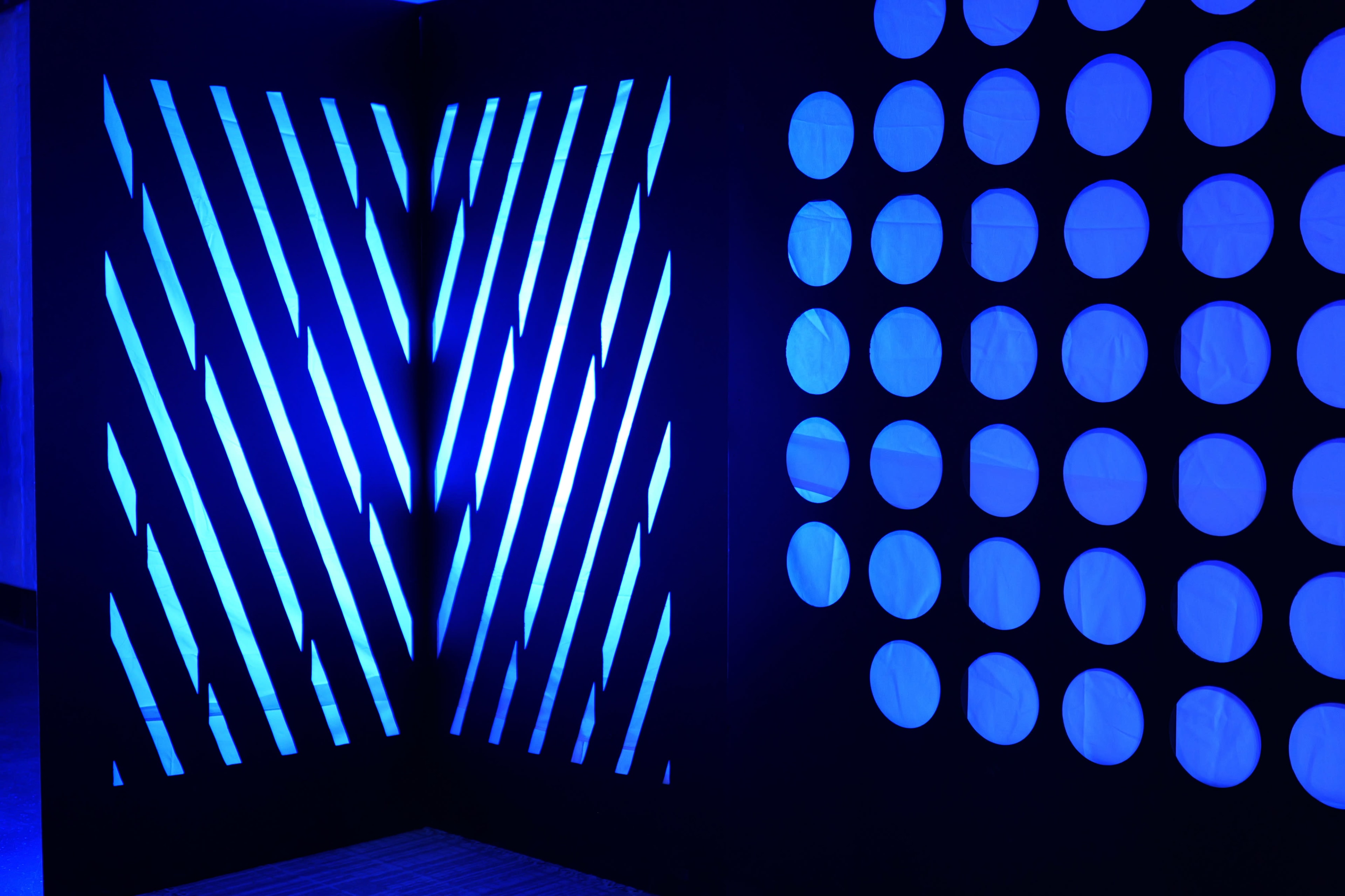 A corner with blue light casting diagonal stripes on one wall and circular cutouts on the adjacent wall, creating contrasting patterns.