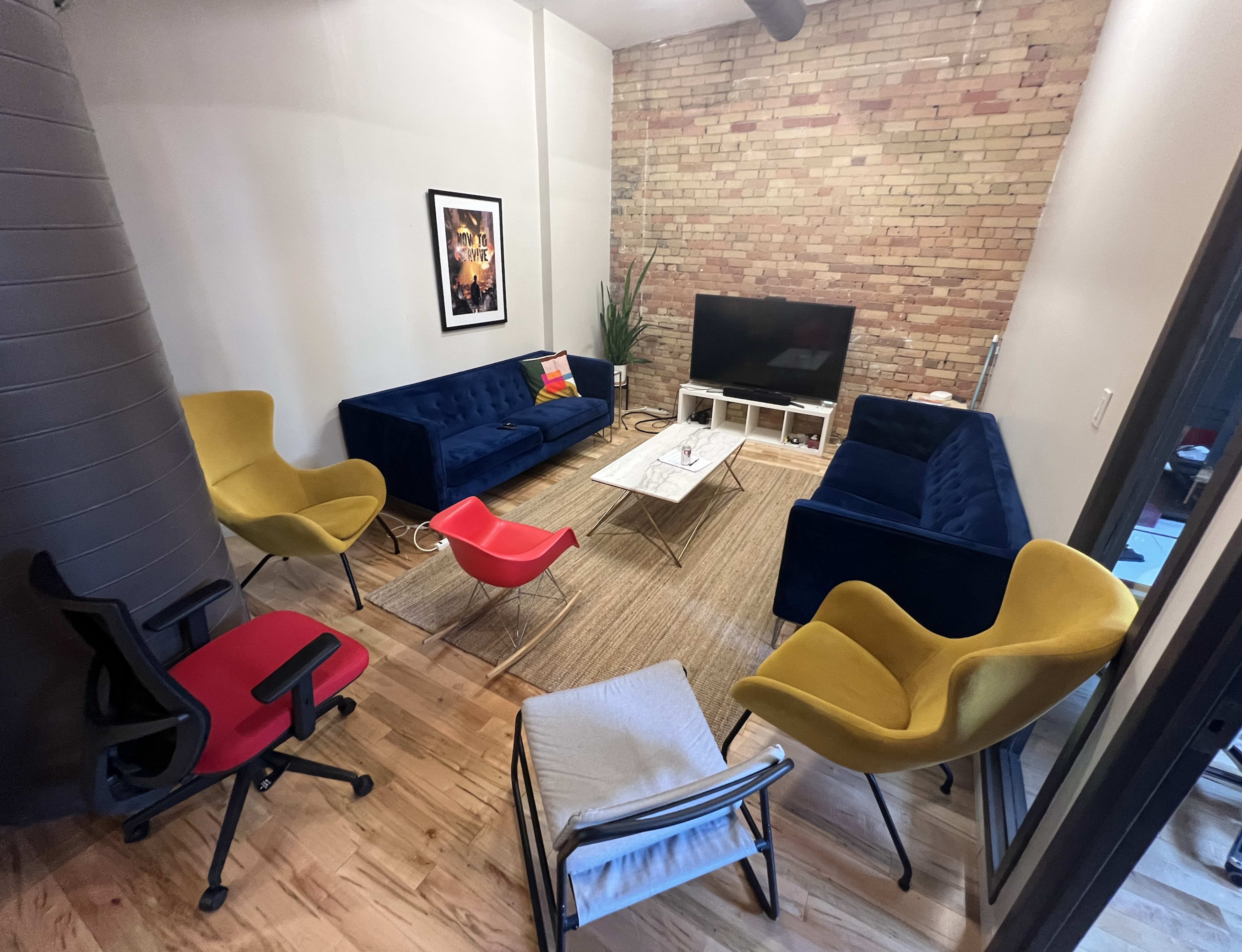 A modern lounge area features blue and yellow seating, a television on a white stand, and a textured brick wall.