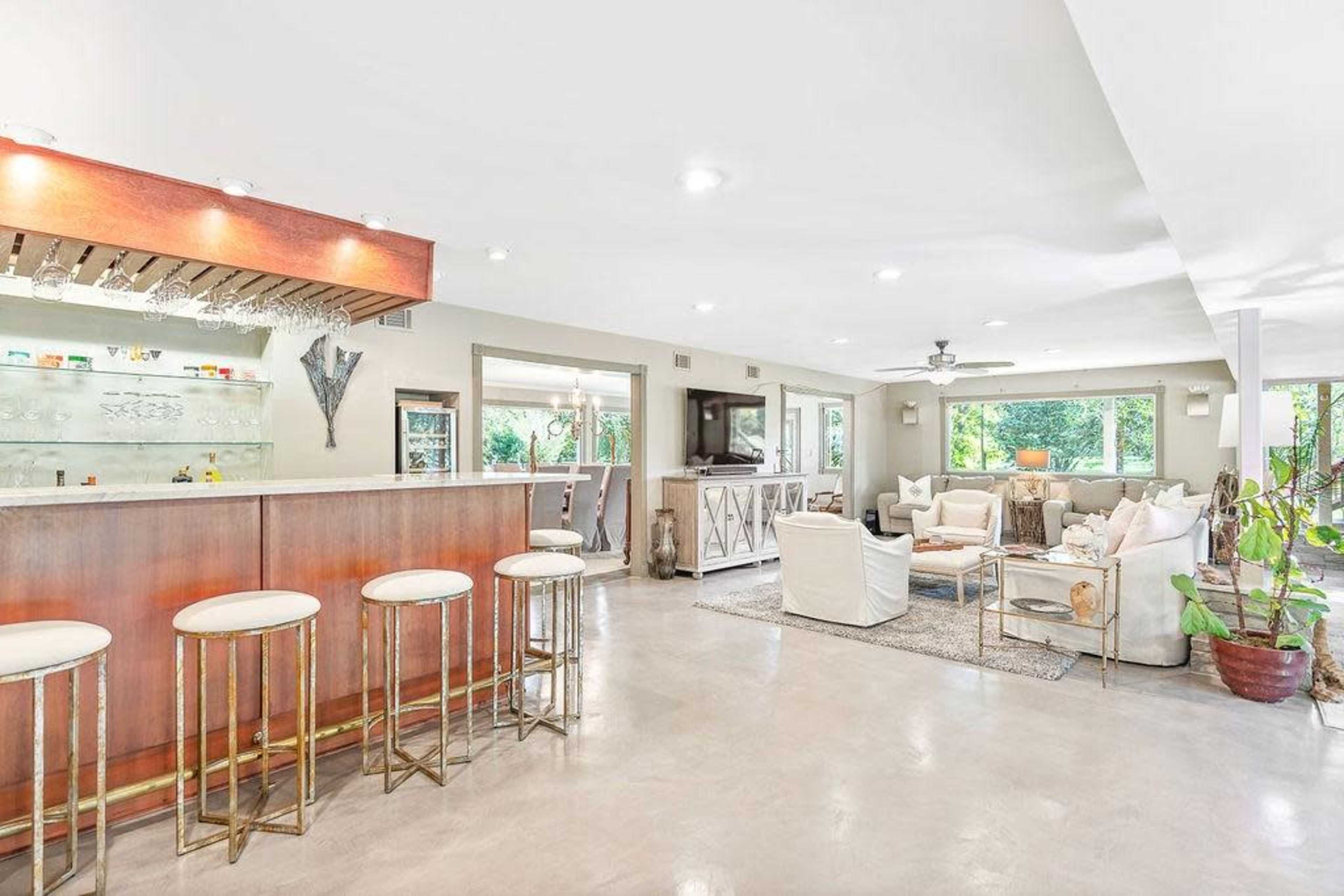 A spacious living area with a bar counter, seating arrangements, and large windows letting in natural light.