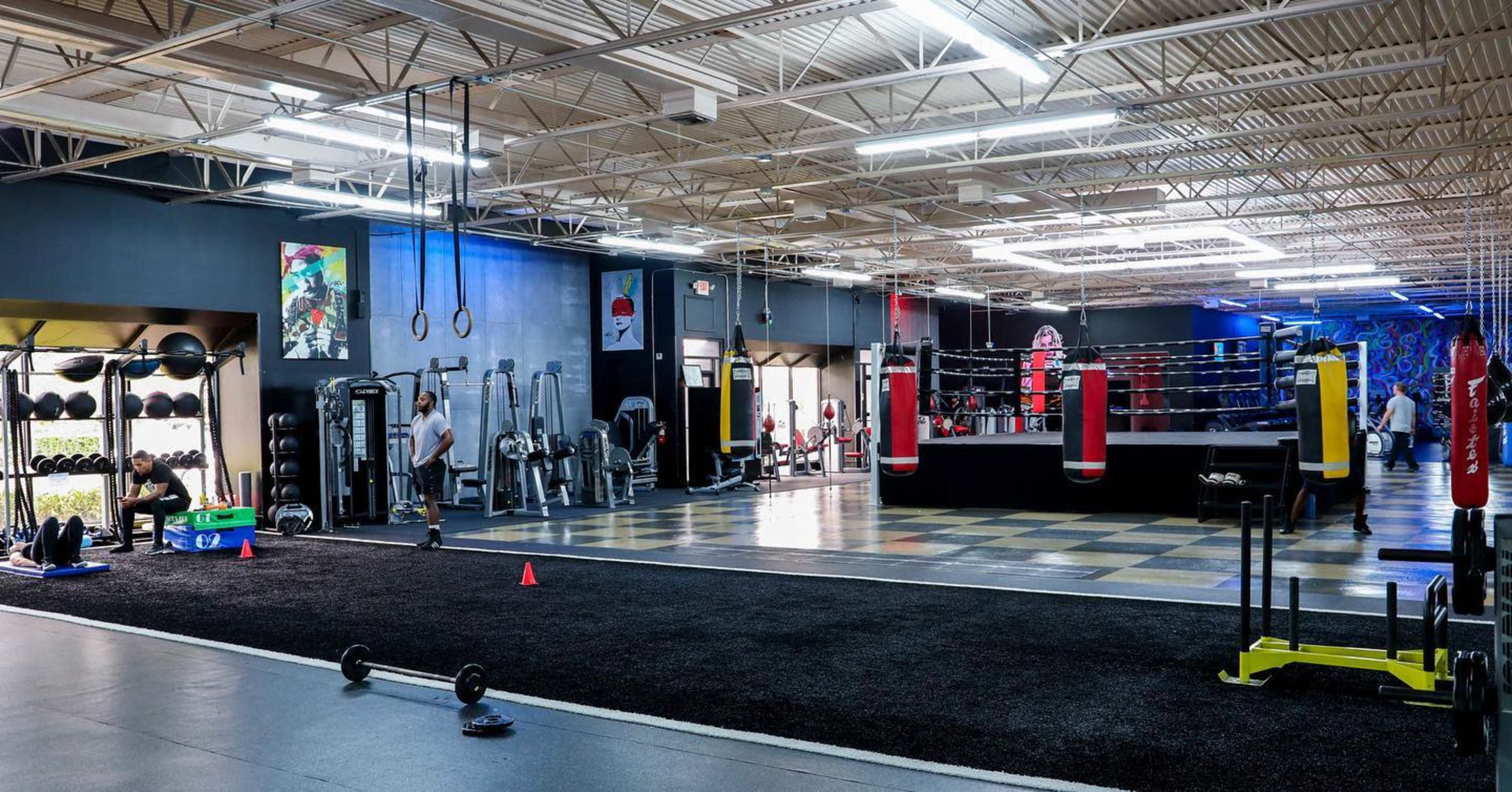 A spacious gym with various workout equipment, including weights, a boxing ring, and exercise mats.