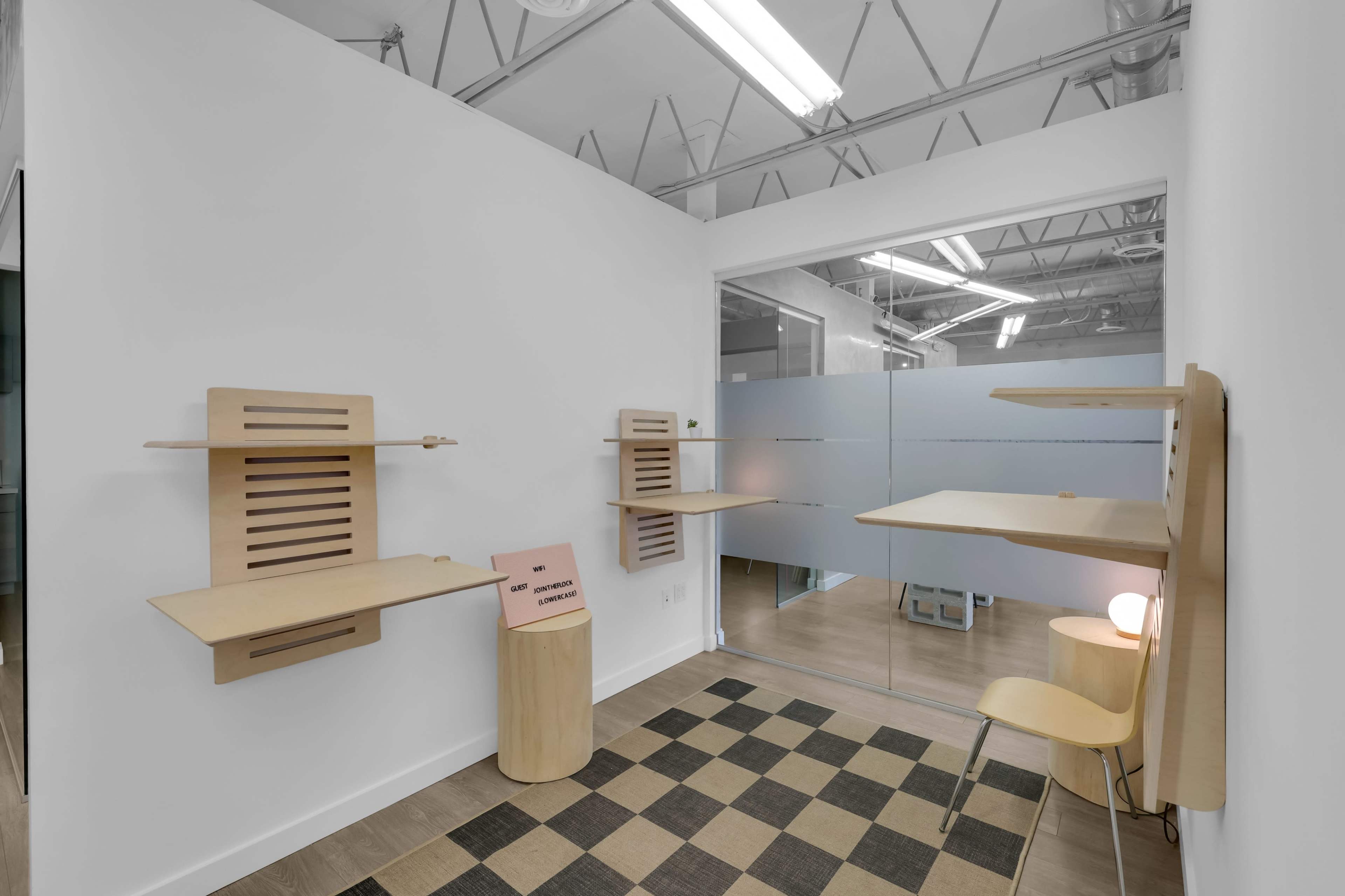 The image shows a minimalist room with wooden shelves mounted on the walls, a small round table, a chair, and a checkered floor.