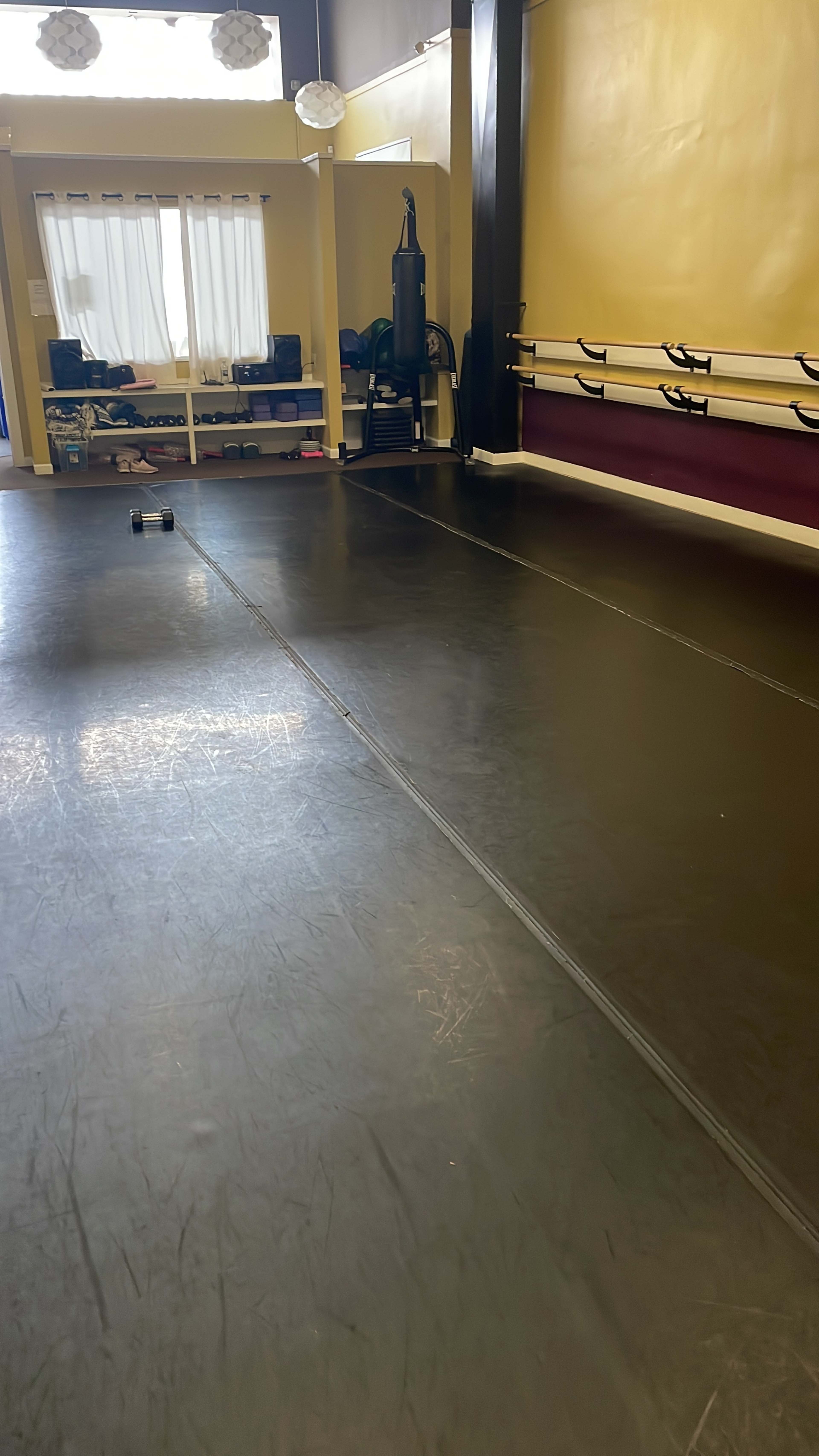 The image shows a spacious gym or studio with a black rubber floor, equipped with exercise equipment and a mirror along one wall.