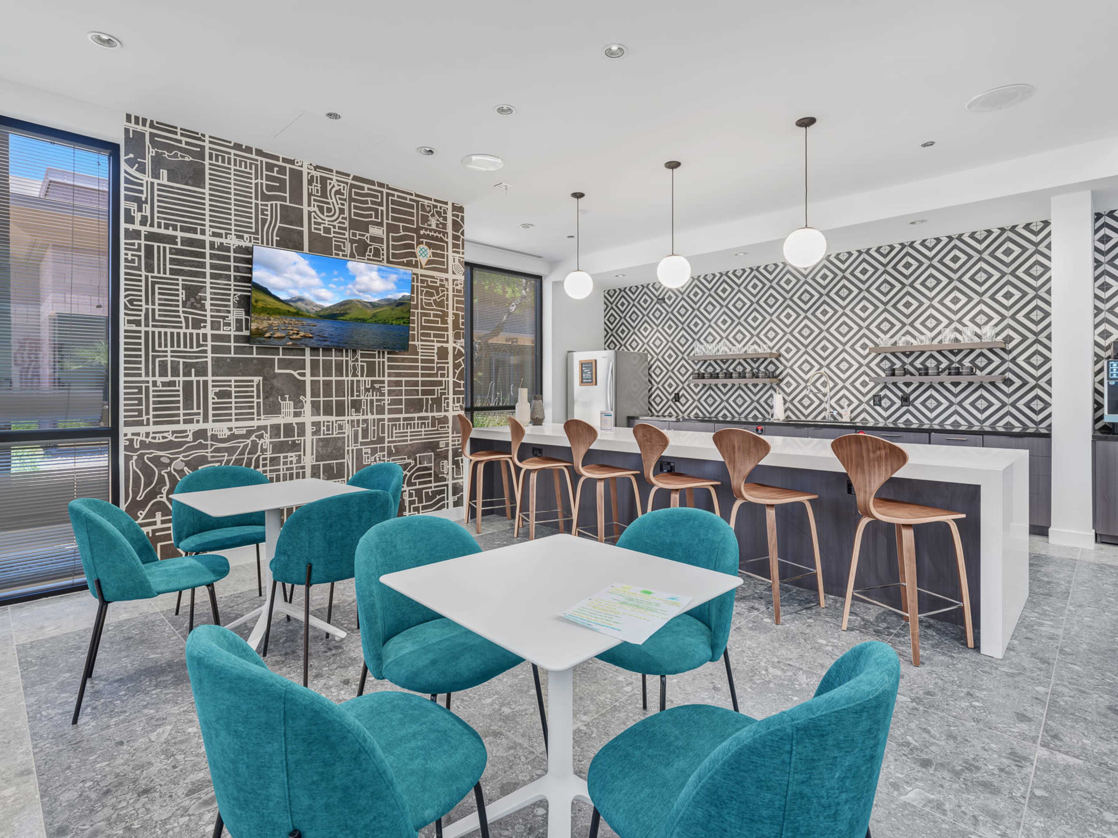 The image shows a modern kitchen area with a patterned wall, a long bar with high stools, and several tables and chairs.