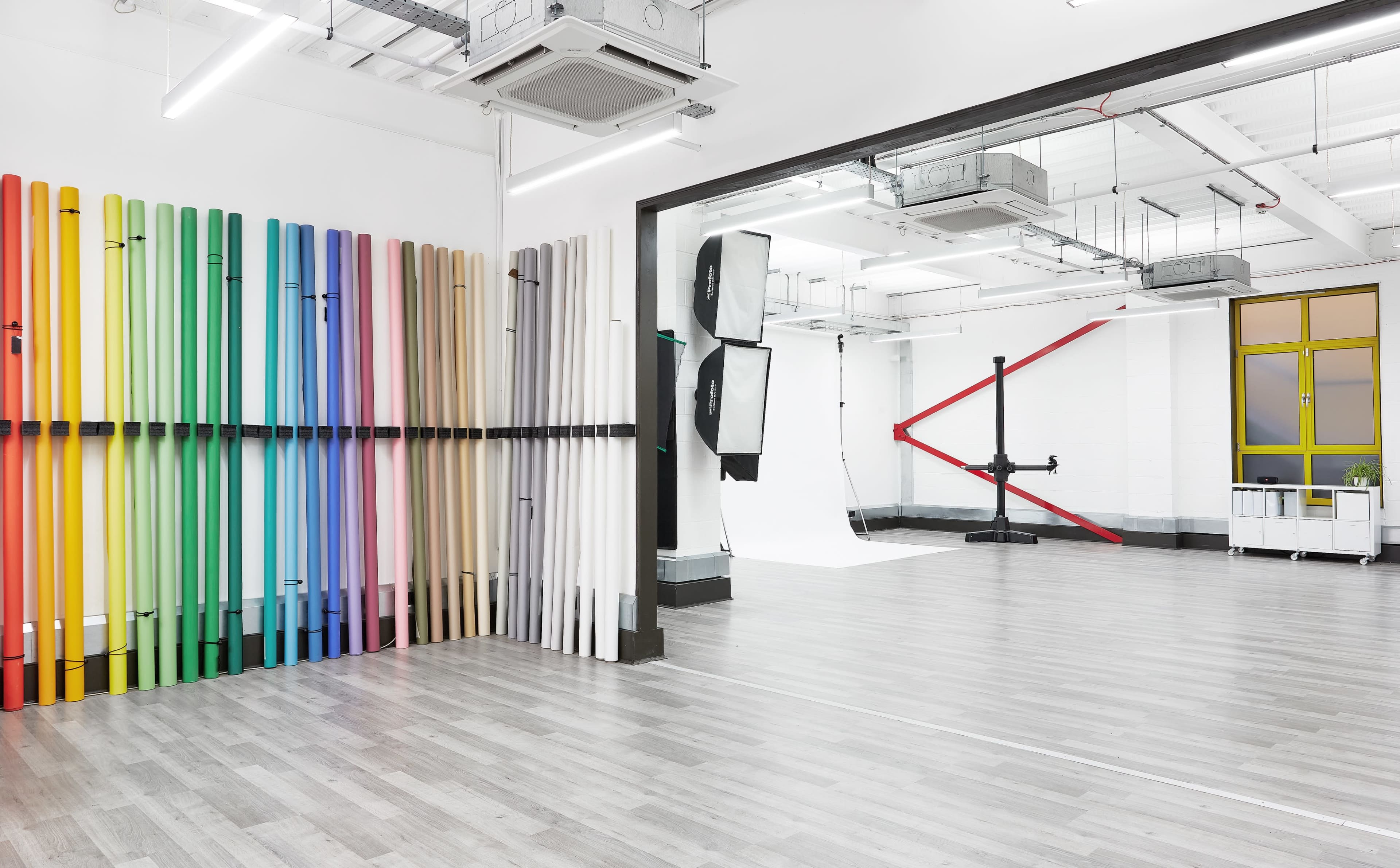 A spacious studio with a wall of colorful backdrops on one side and a photography setup featuring softboxes and a backdrop on the other.
