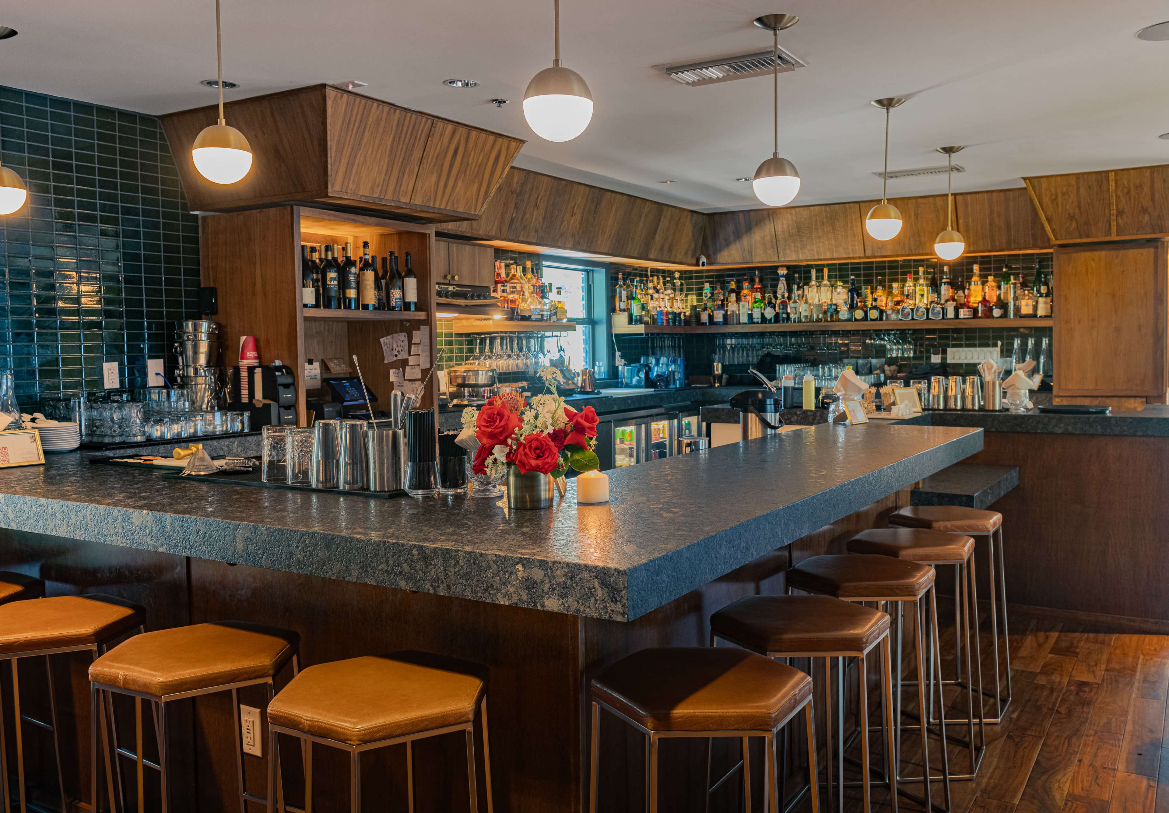 The image shows a well-lit bar area with a long counter, several high stools, and a variety of liquor bottles displayed behind the bar.