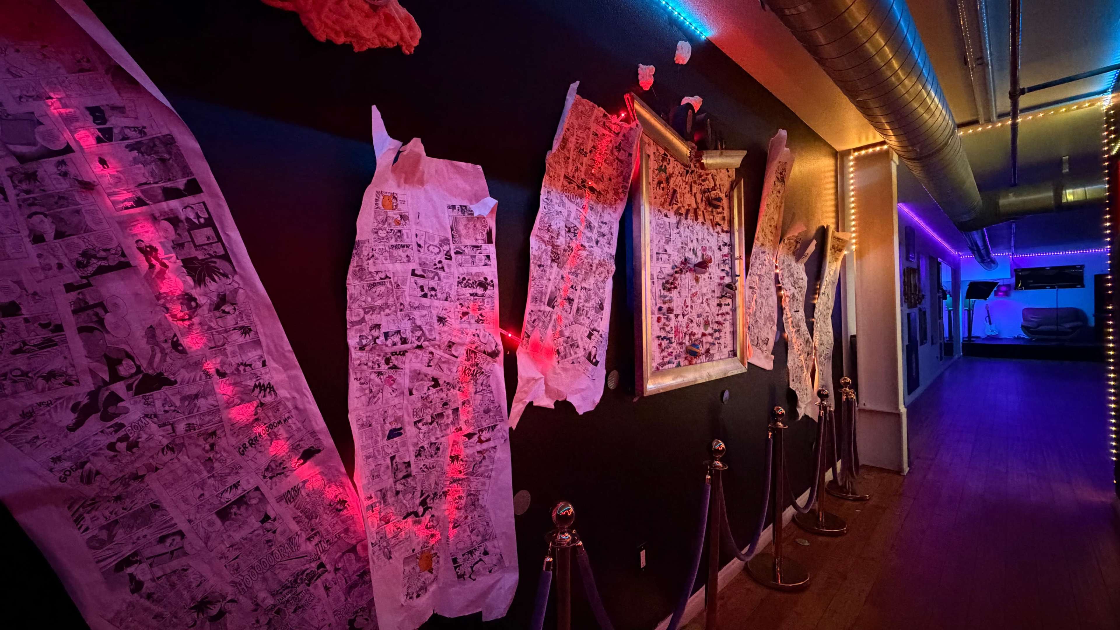 The image shows a hallway with colorful neon lights, featuring several comic strip pages taped to a dark wall.