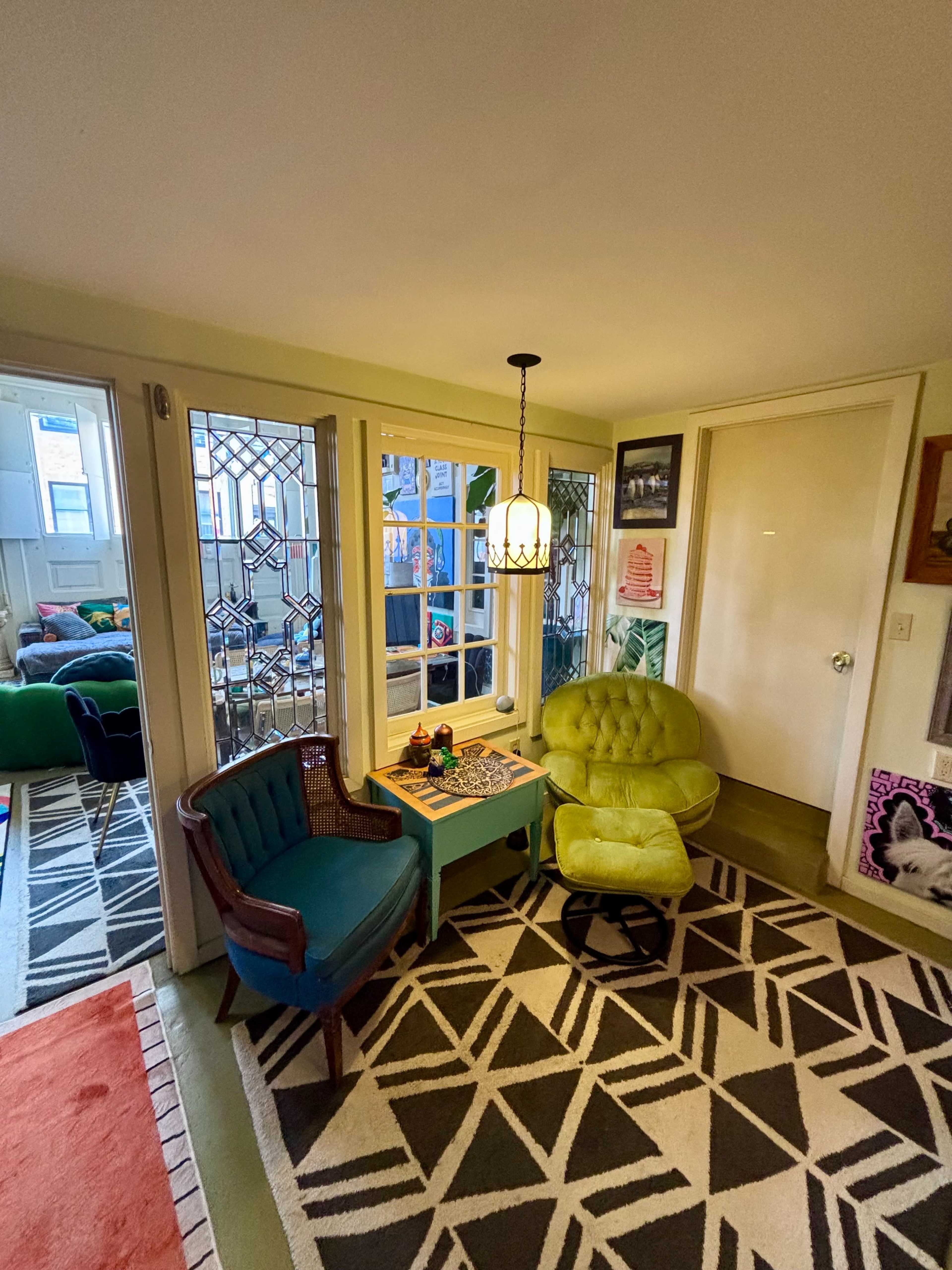 The image shows a cozy interior space featuring two chairs, a small table, and large windows with decorative glass.