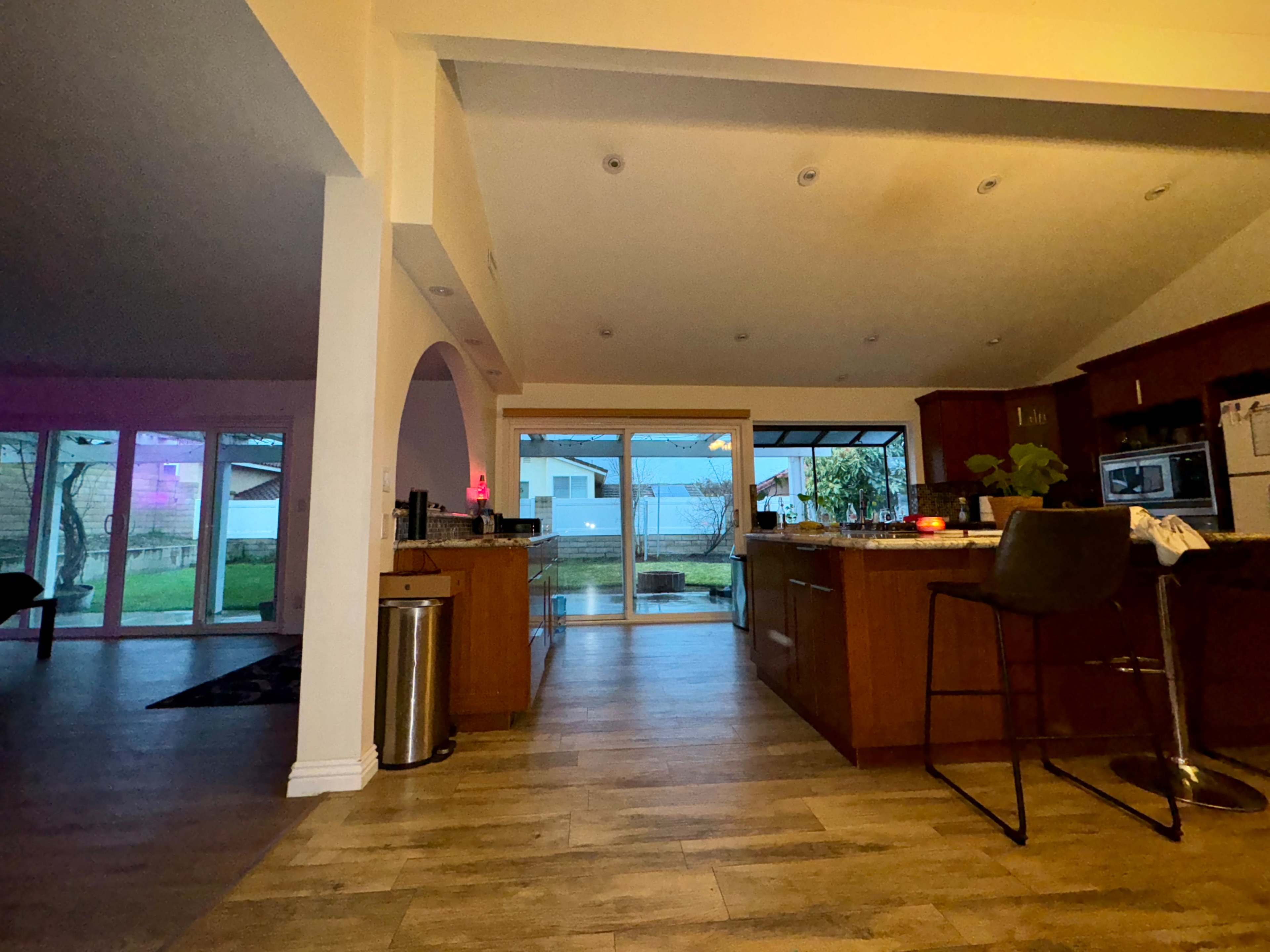 A kitchen with wooden cabinets and a bar stool, leading to a view of a patio and backyard through large sliding glass doors.