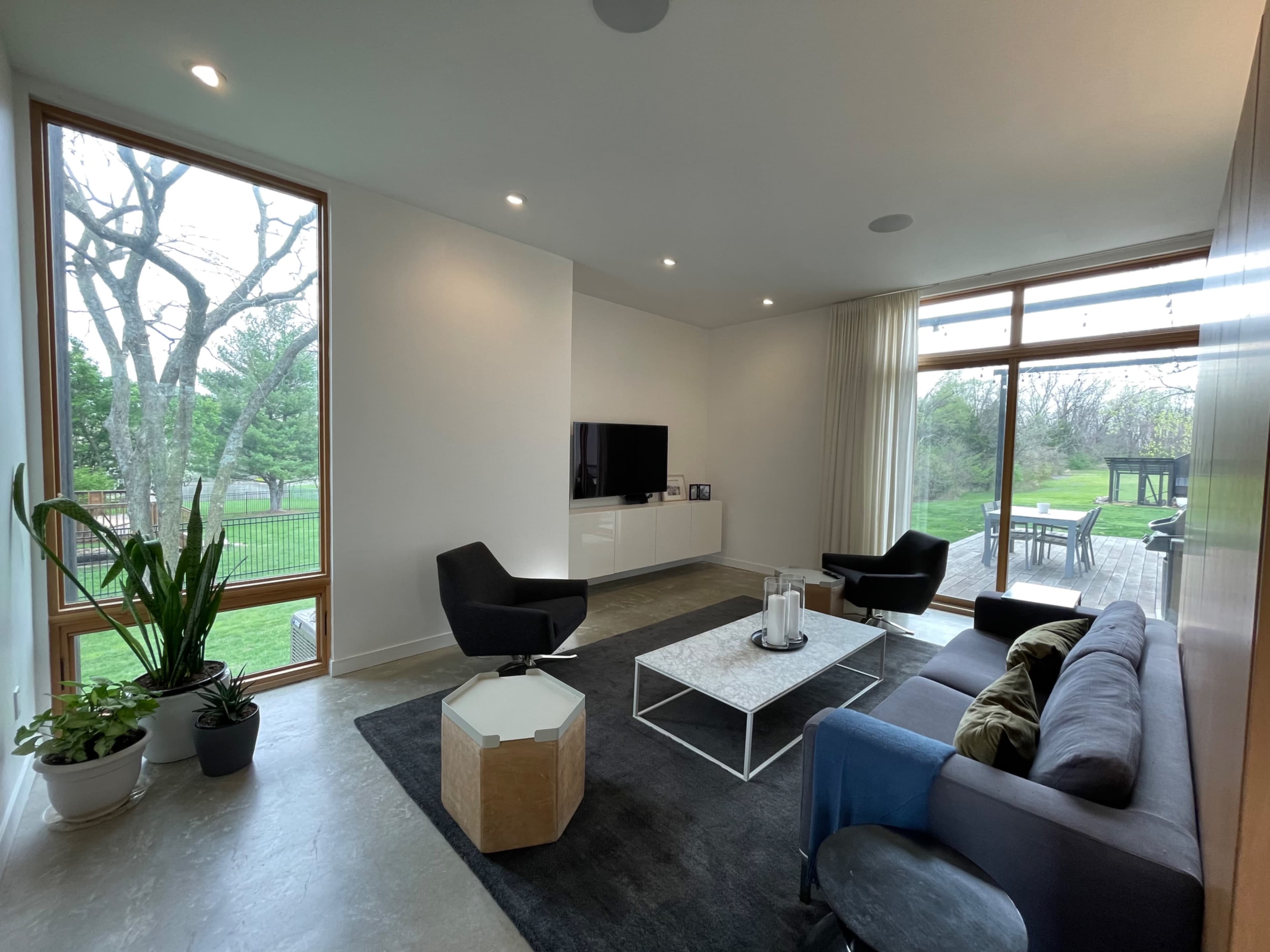 The living room features a modern design with a sofa, armchairs, a coffee table, and a large window overlooking the outdoor area.