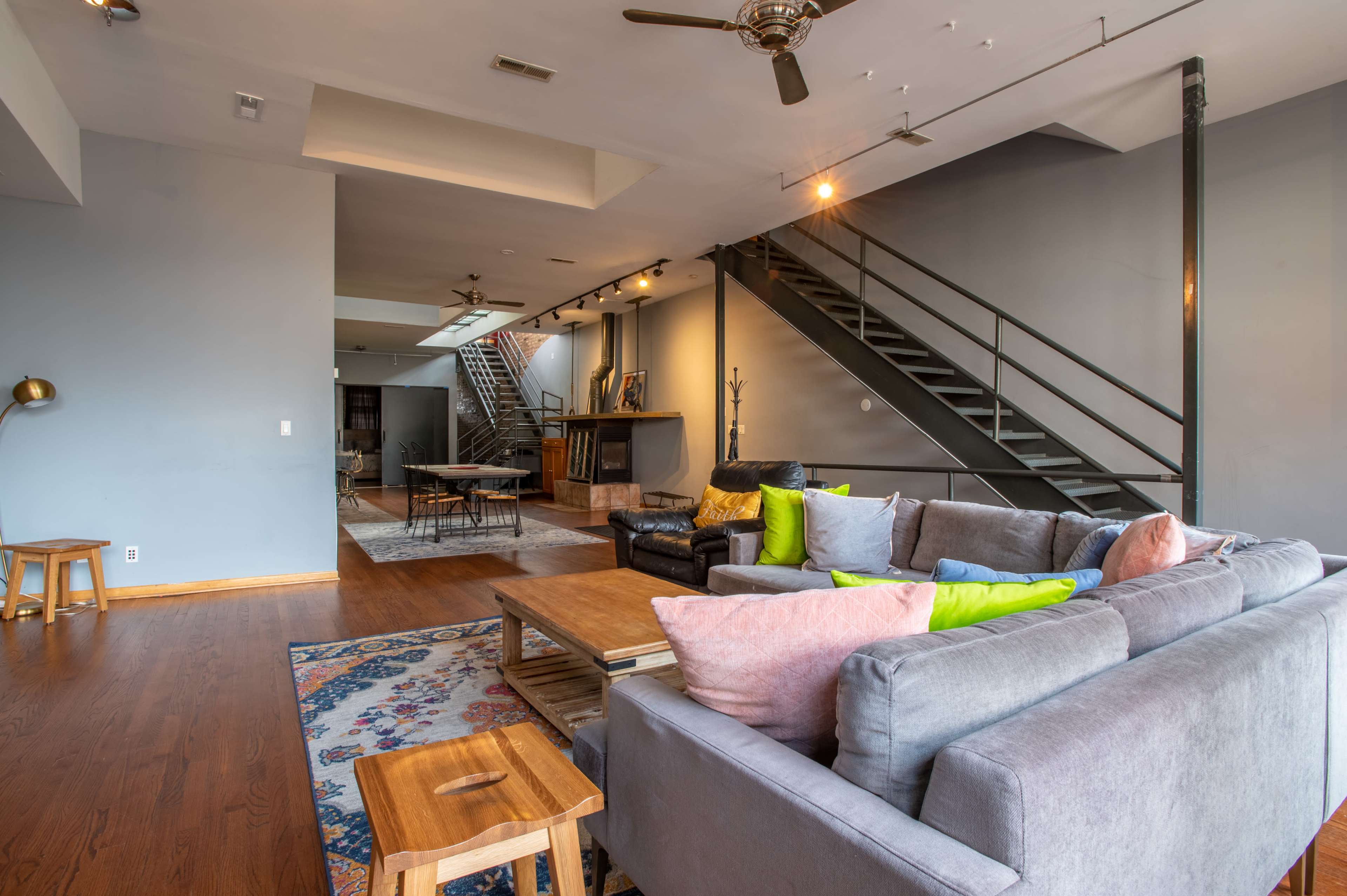 A spacious living area features a sectional sofa, wooden coffee table, and a large staircase leading to an upper level.