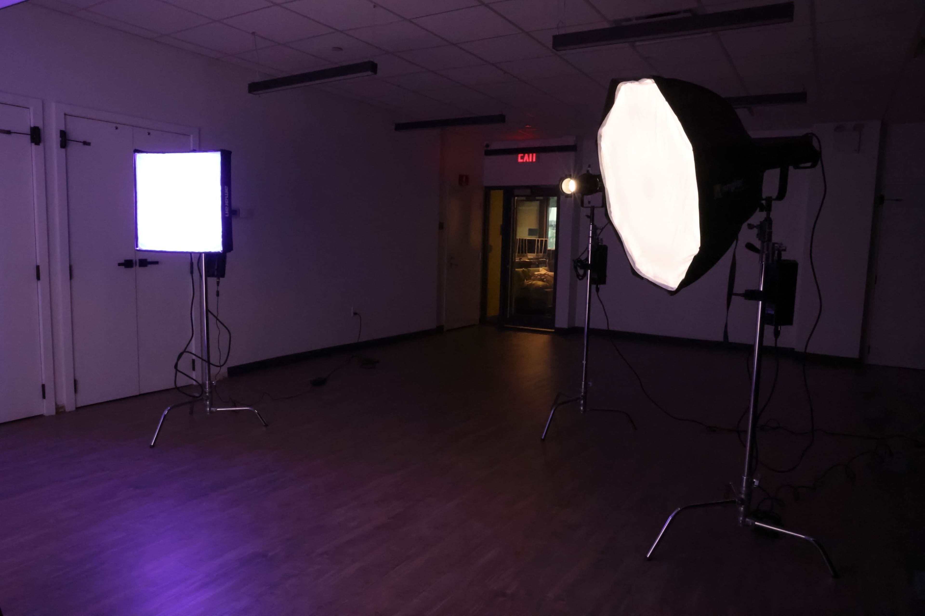 The image shows a dimly lit studio space with two lighting setups: a square softbox on the left and an octagonal softbox on the right.