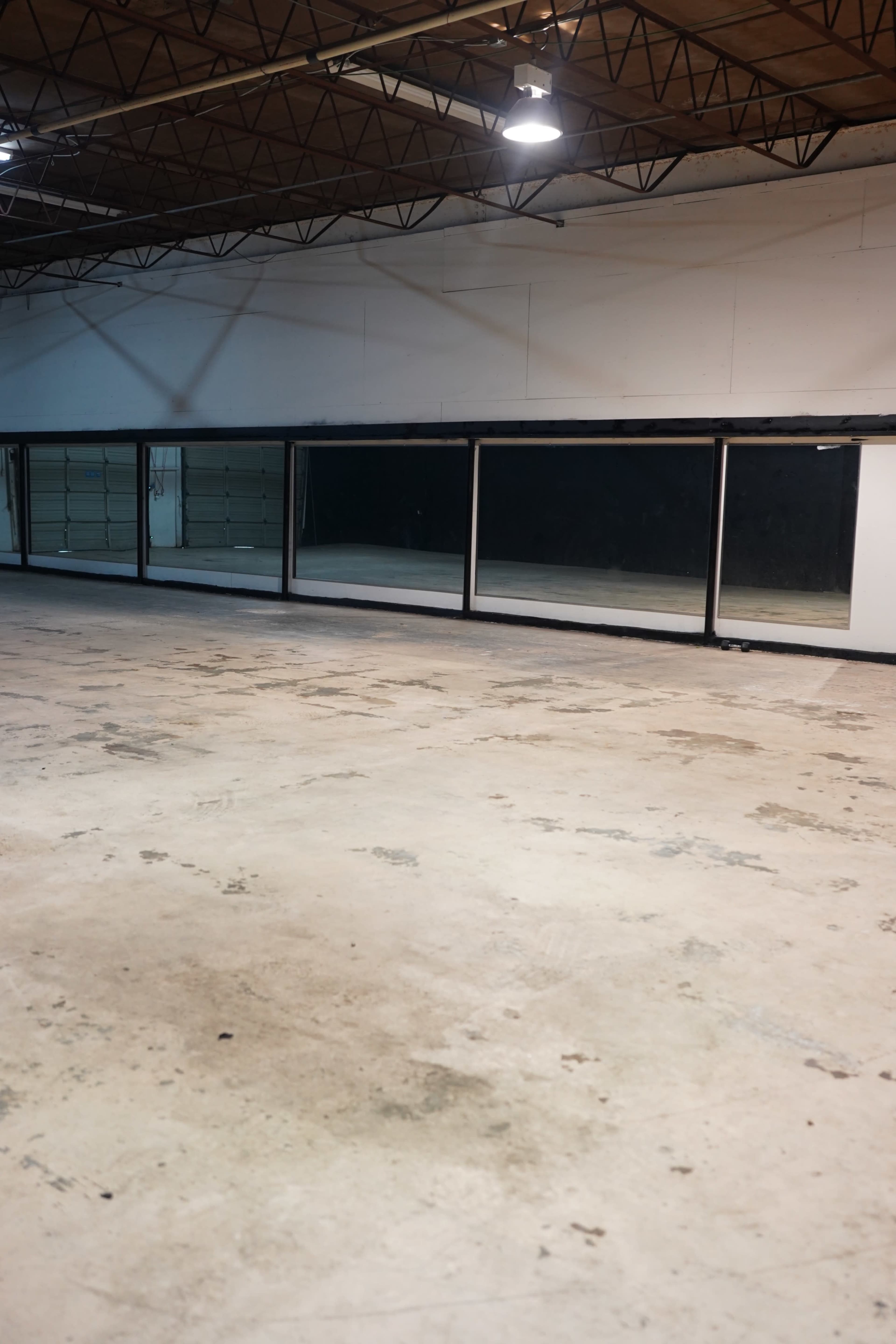 The image shows an empty warehouse interior with a concrete floor and large windows along one wall.