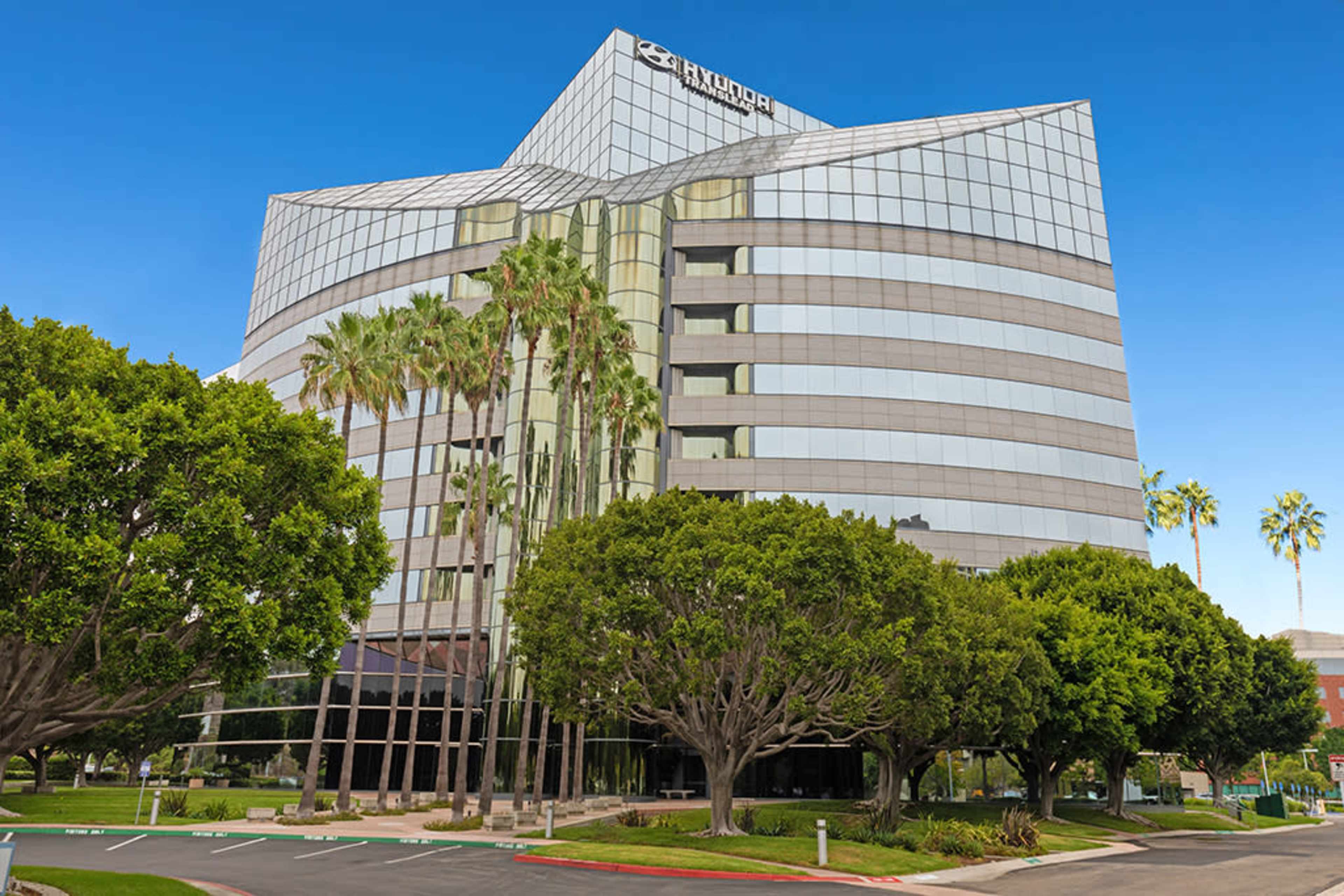 The image shows a modern glass office building surrounded by palm trees and landscaped greenery.